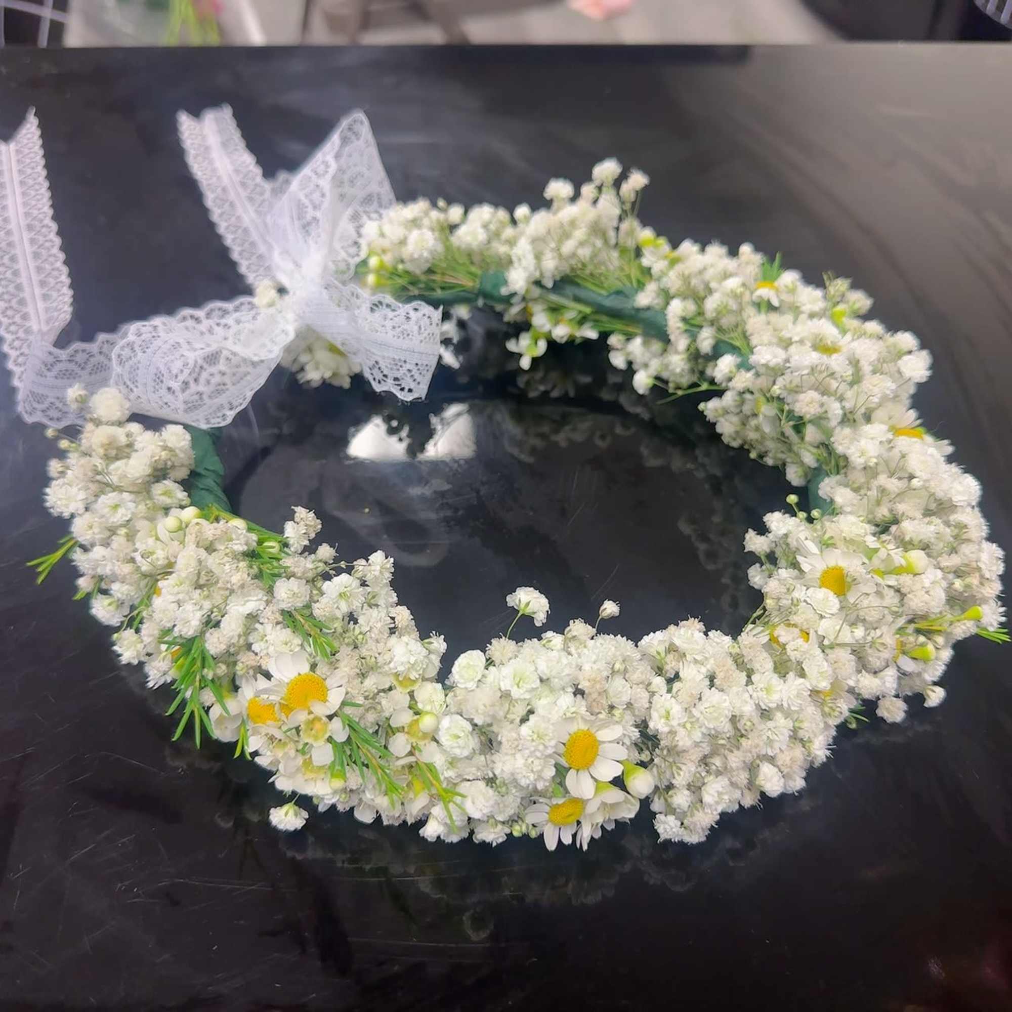 White floral wreath with lace ribbon accents and small daisy flowers