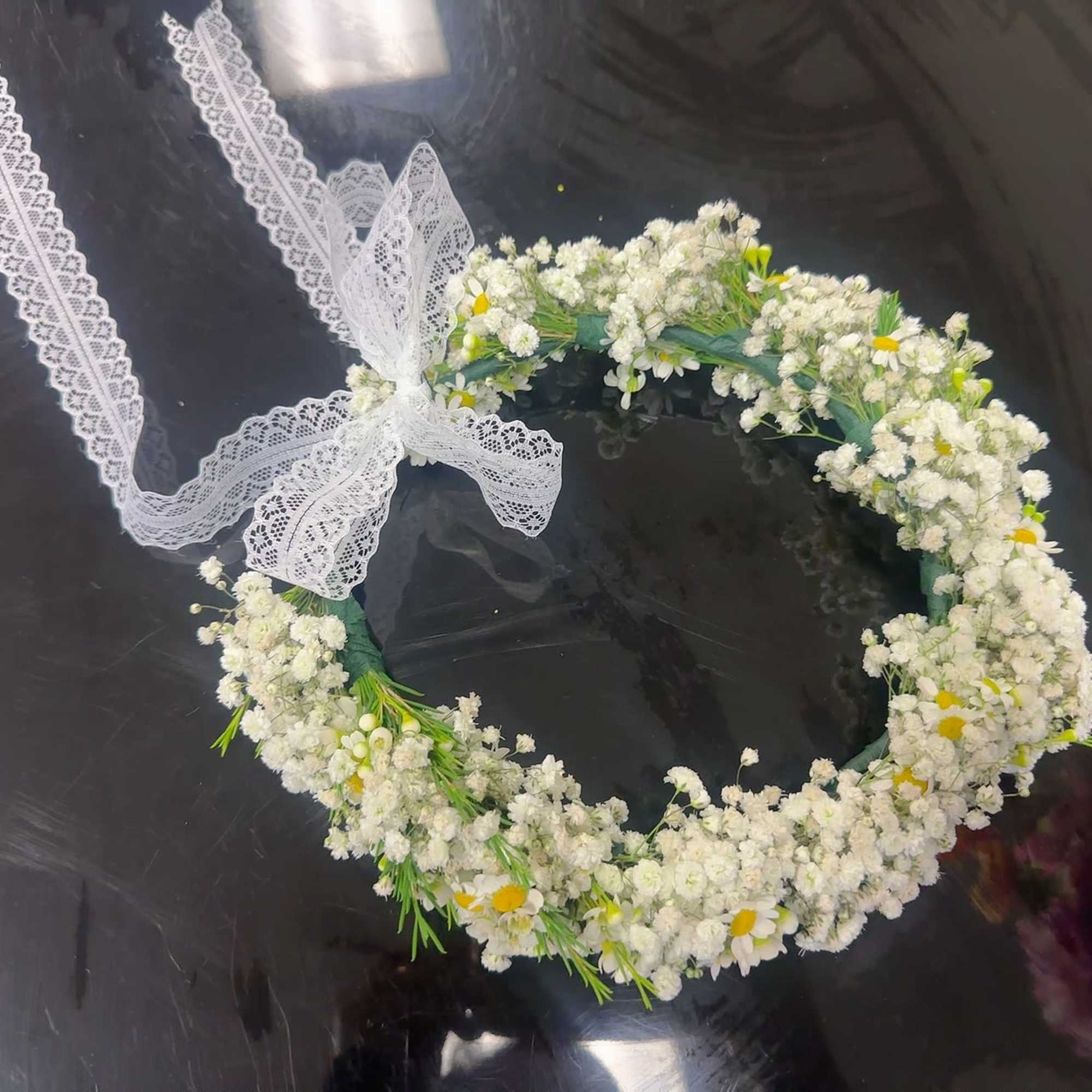 White floral wreath with a lace ribbon bow on a dark surface