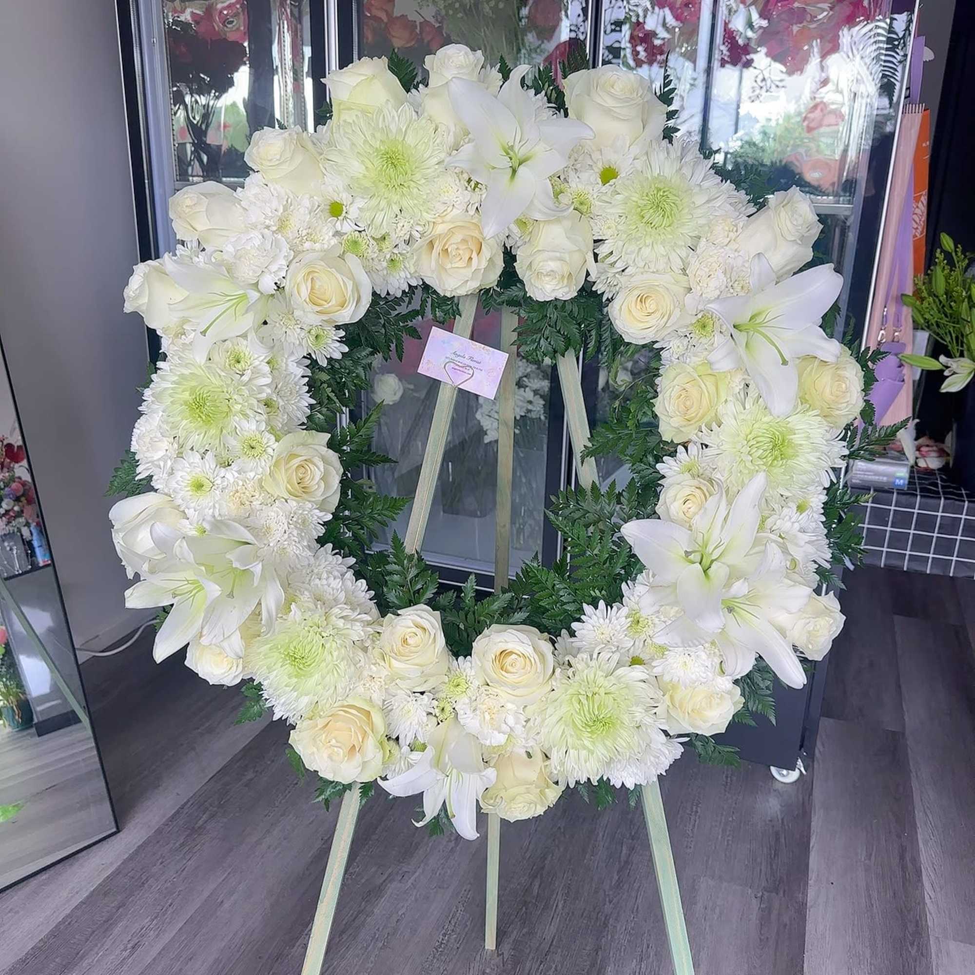 White floral wreath on a standing easel with roses and lilies