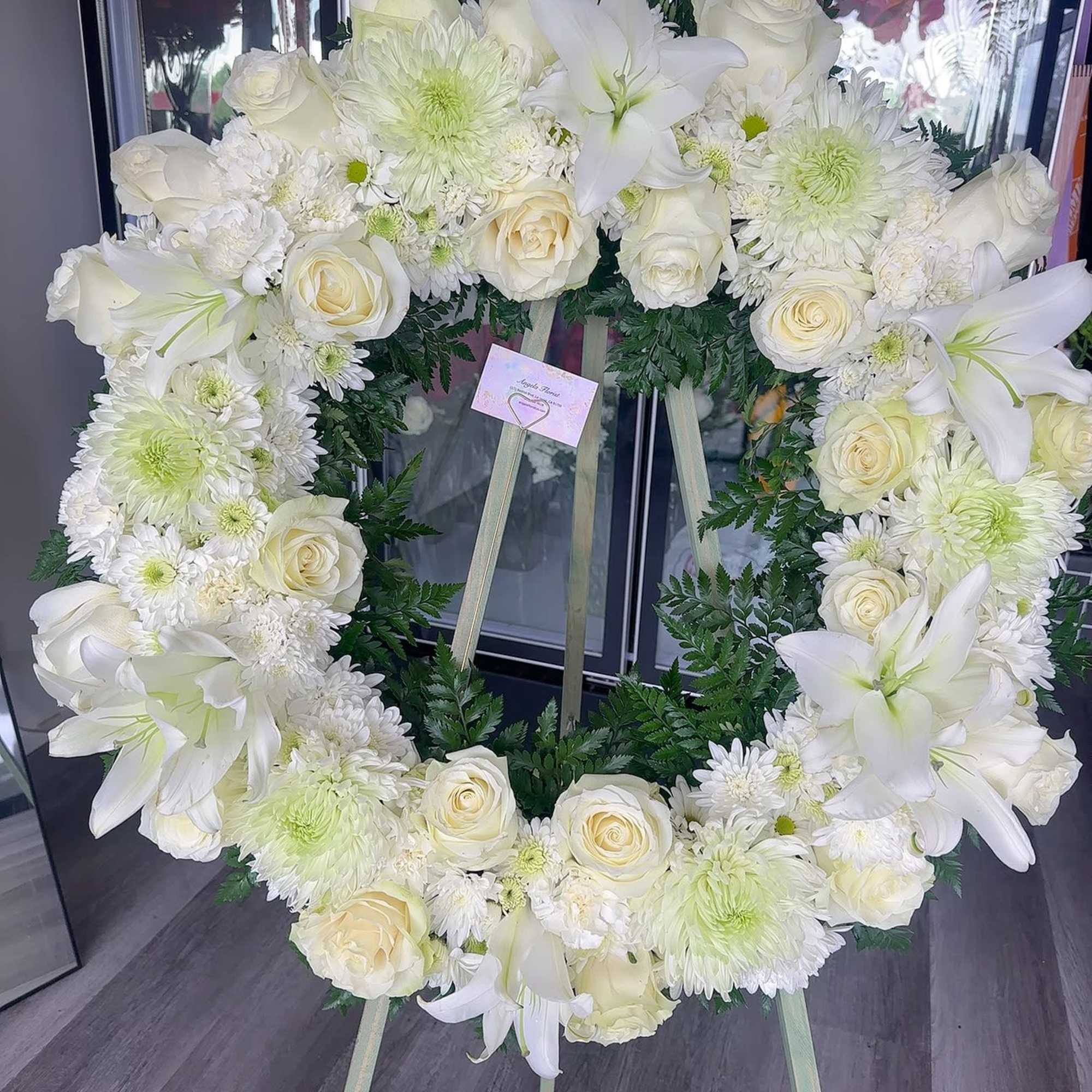 White floral wreath on an easel with roses, lilies, and chrysanthemums