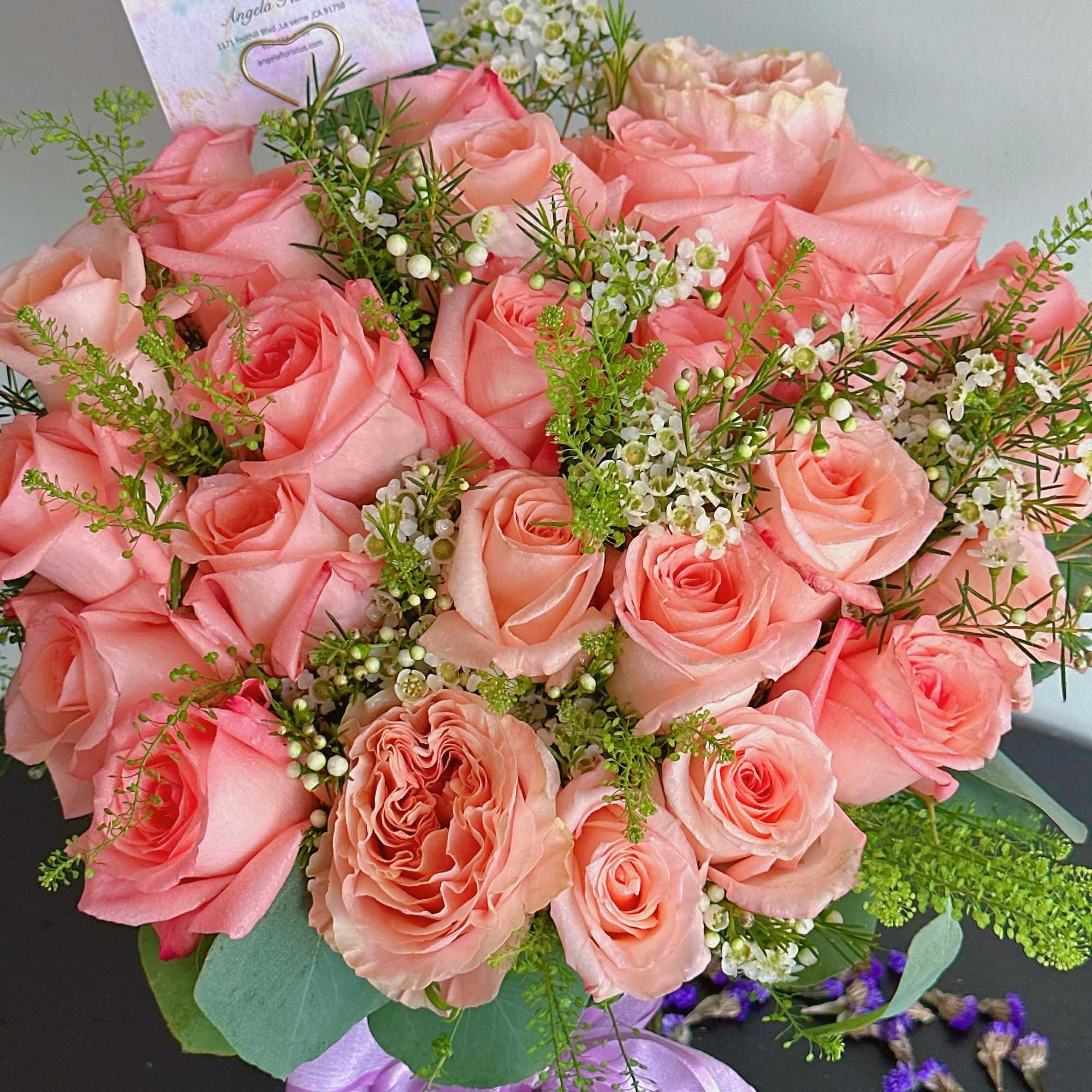 Pink rose bouquet with white filler flowers and a purple ribbon