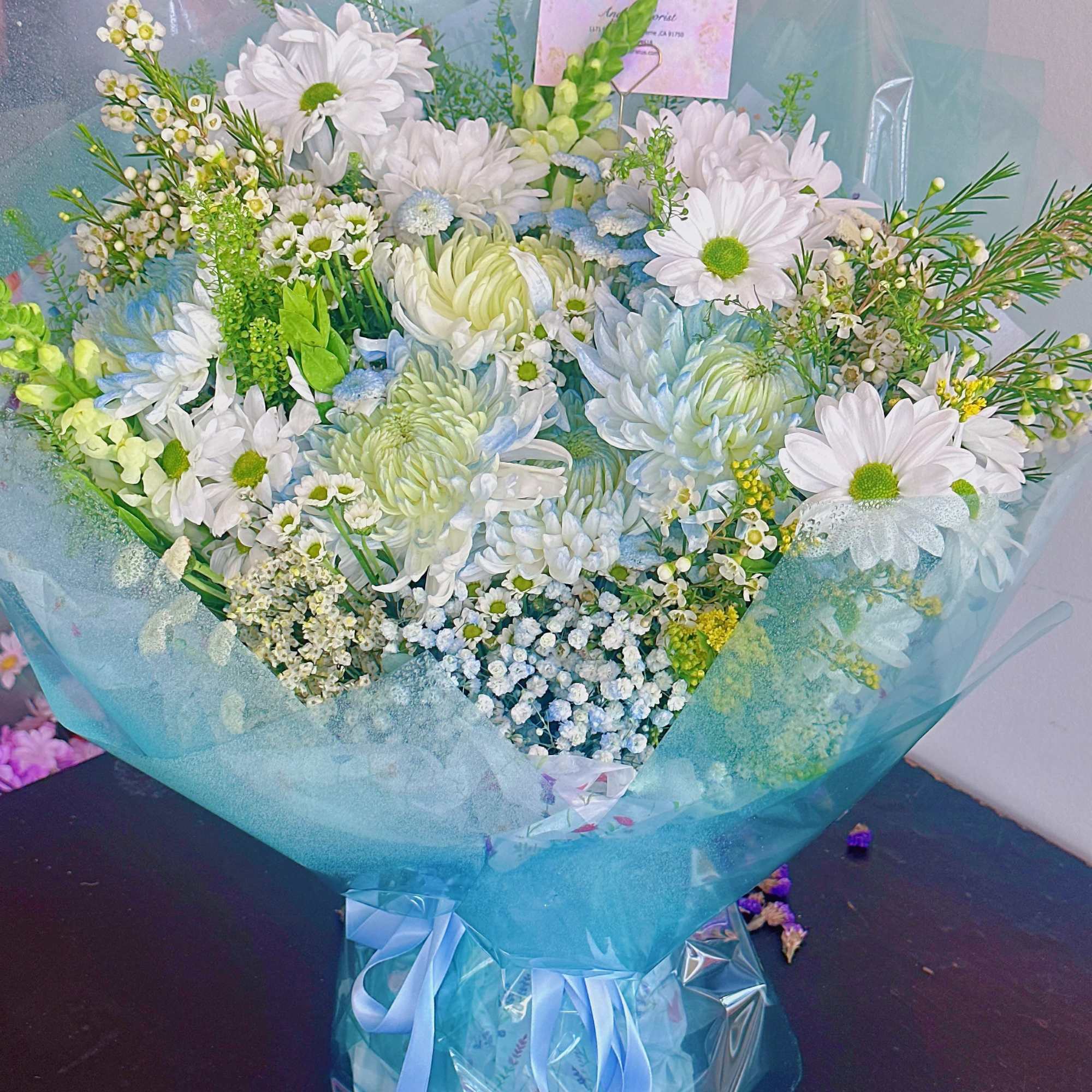 Bouquet of white and pale blue flowers wrapped in blue paper