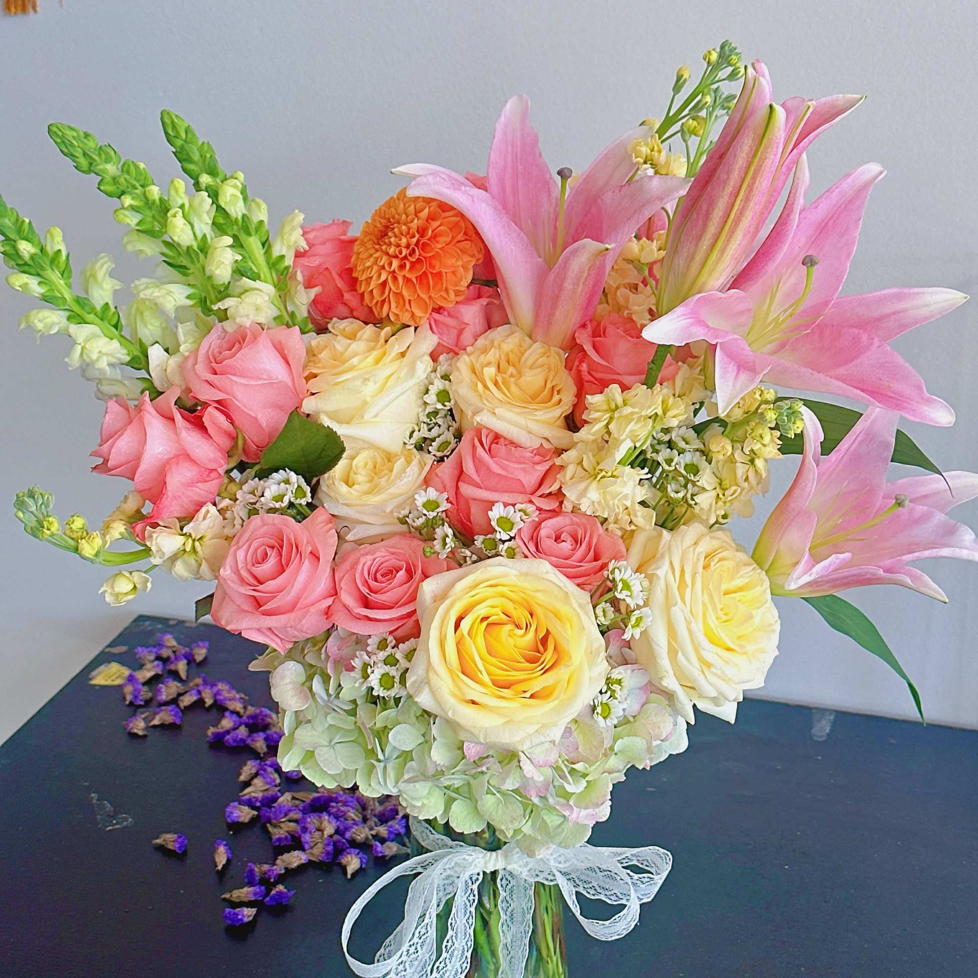 Pink and yellow roses with lilies in a glass vase