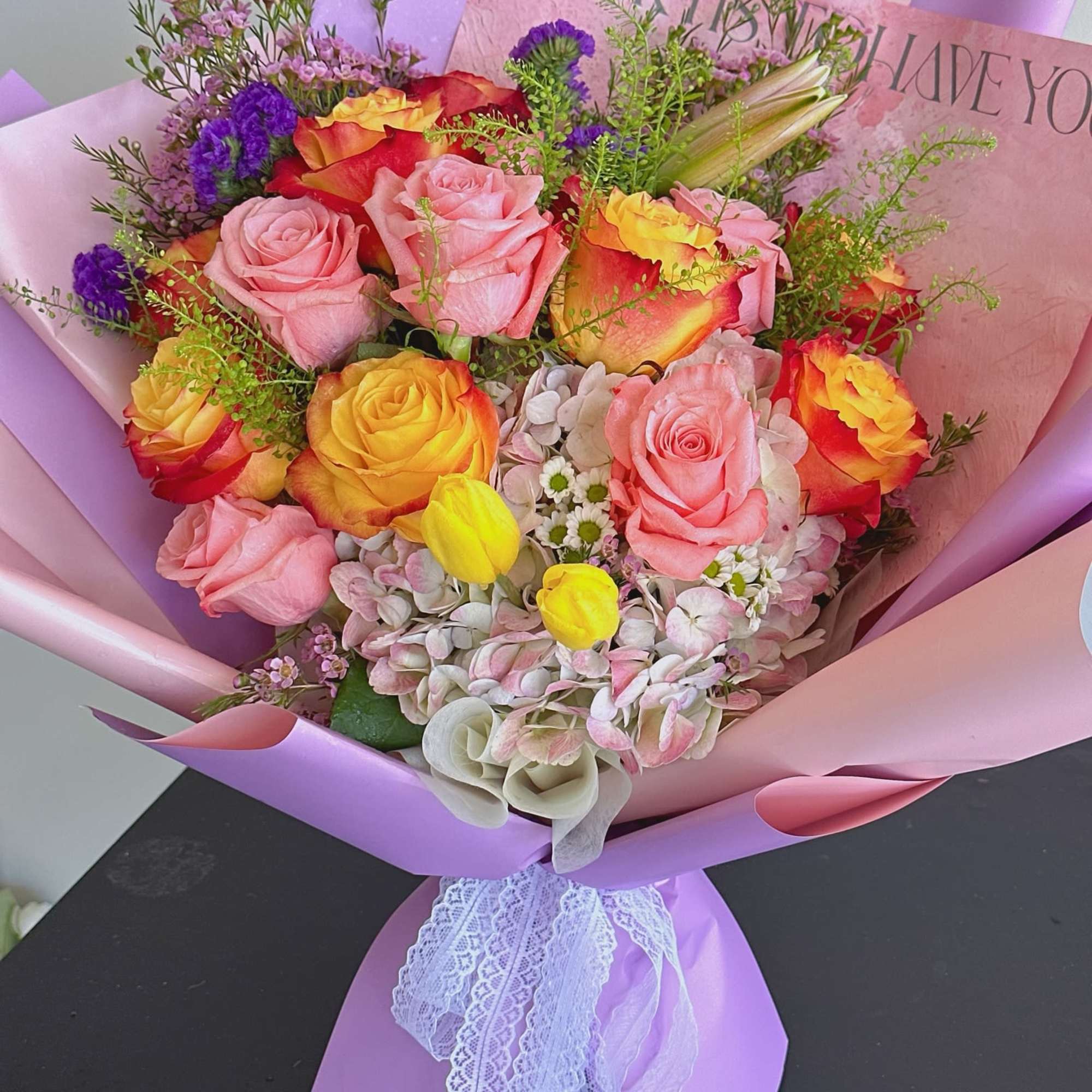 Bouquet of pink and yellow roses wrapped in lavender paper