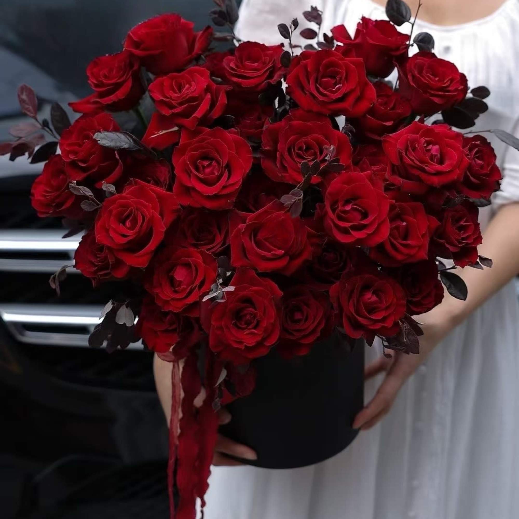 Bouquet of red roses in a black box with dark foliage