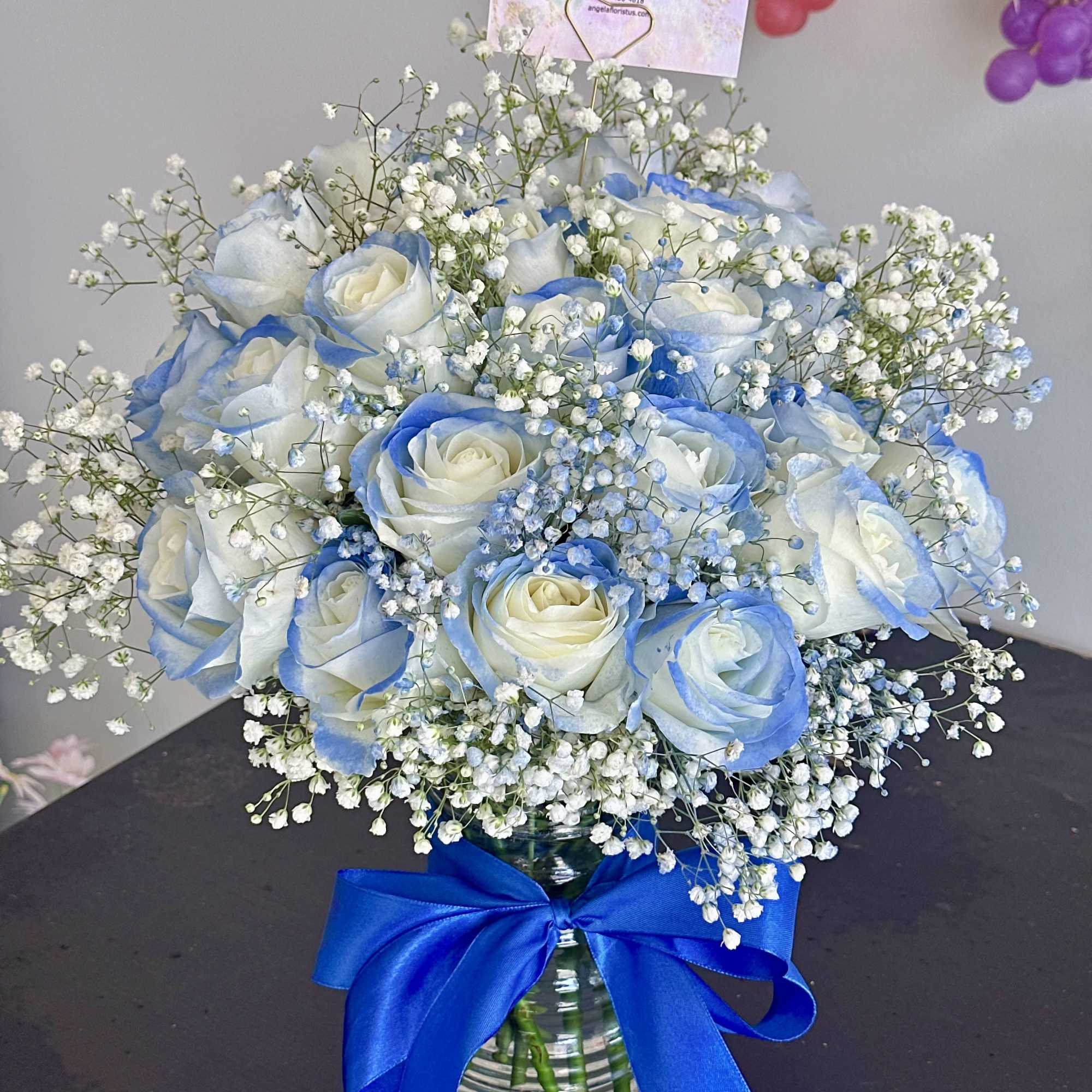 Blue-tinted white rose bouquet in a glass vase with baby's breath and a blue ribbon