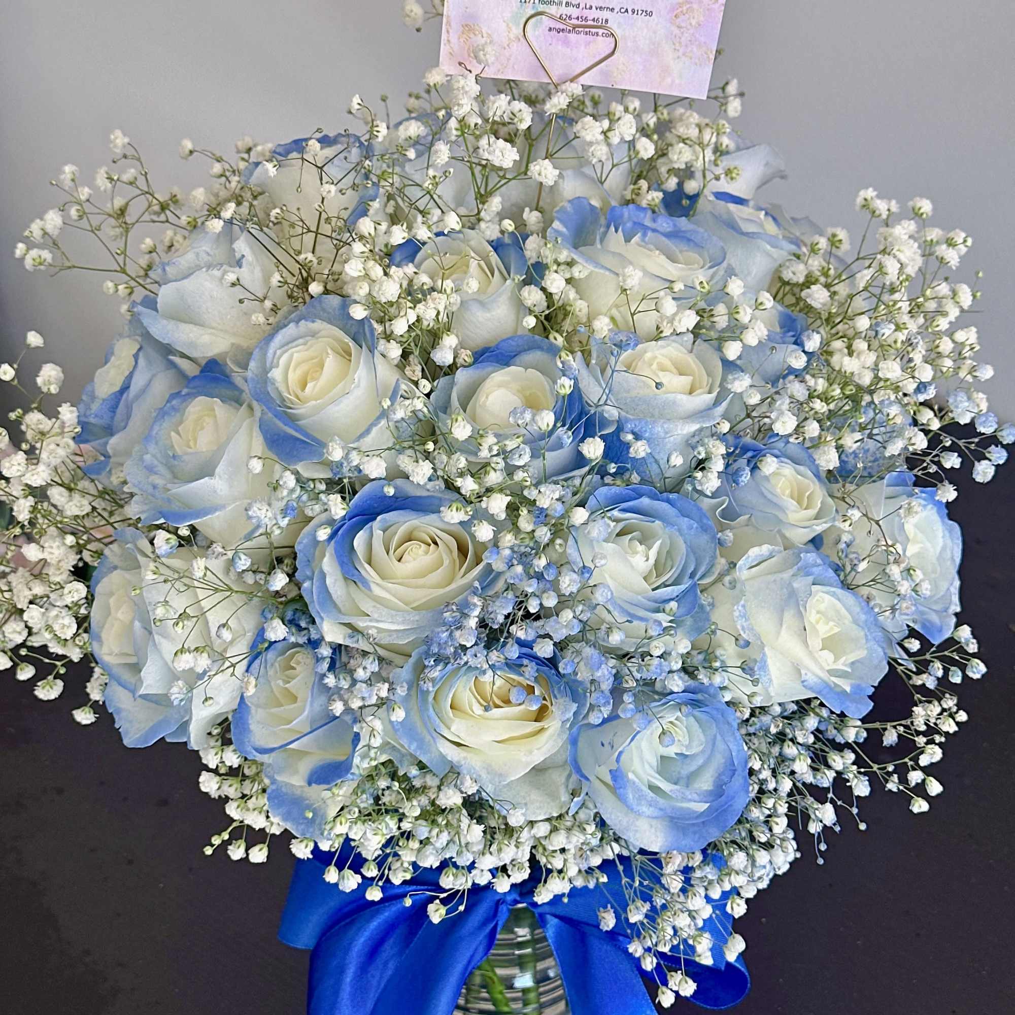 Blue-tinted white roses in a glass vase with baby's breath and a blue ribbon, photo 2 of 4