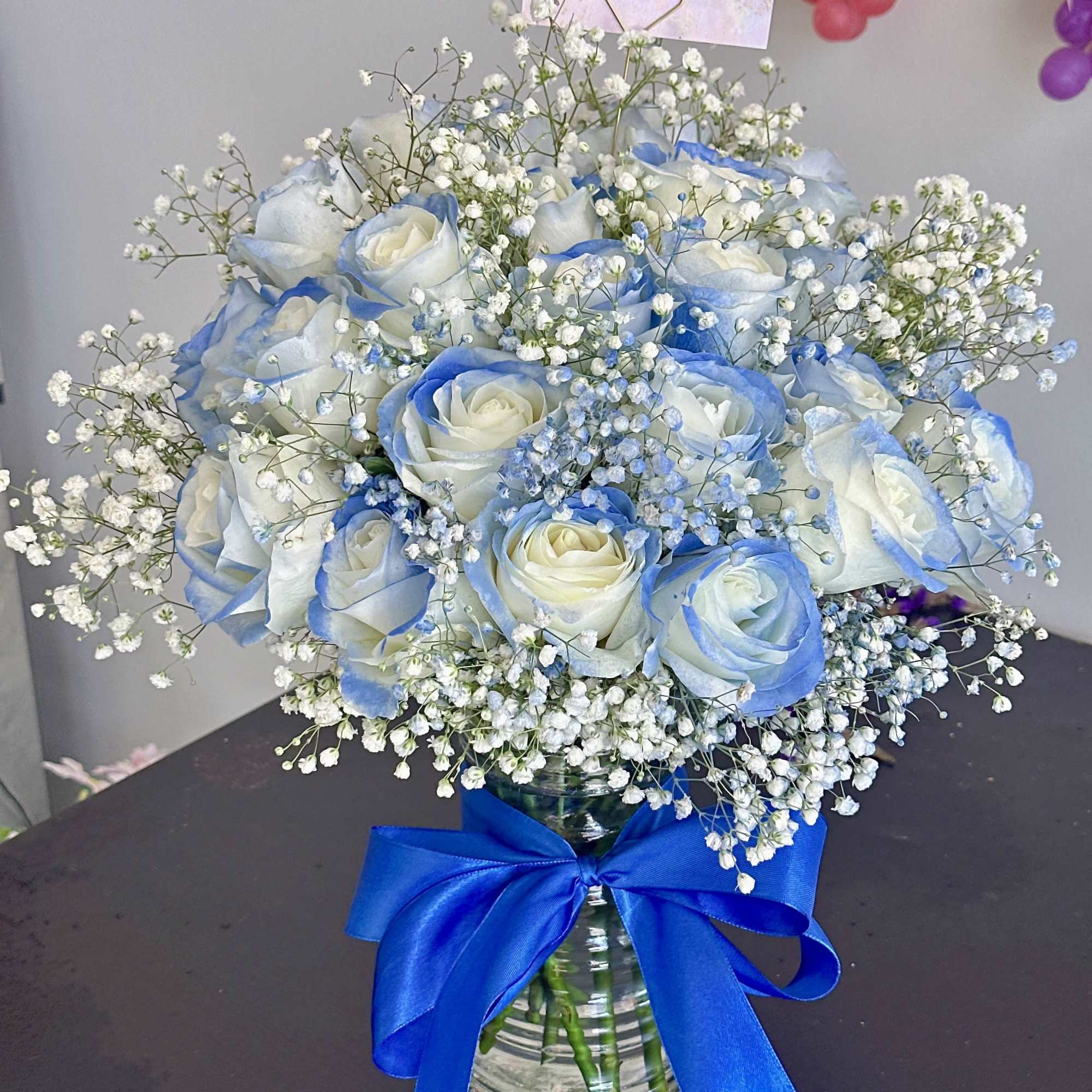 Blue-tinted white roses in a glass vase with baby's breath and a blue ribbon, photo 4 of 4