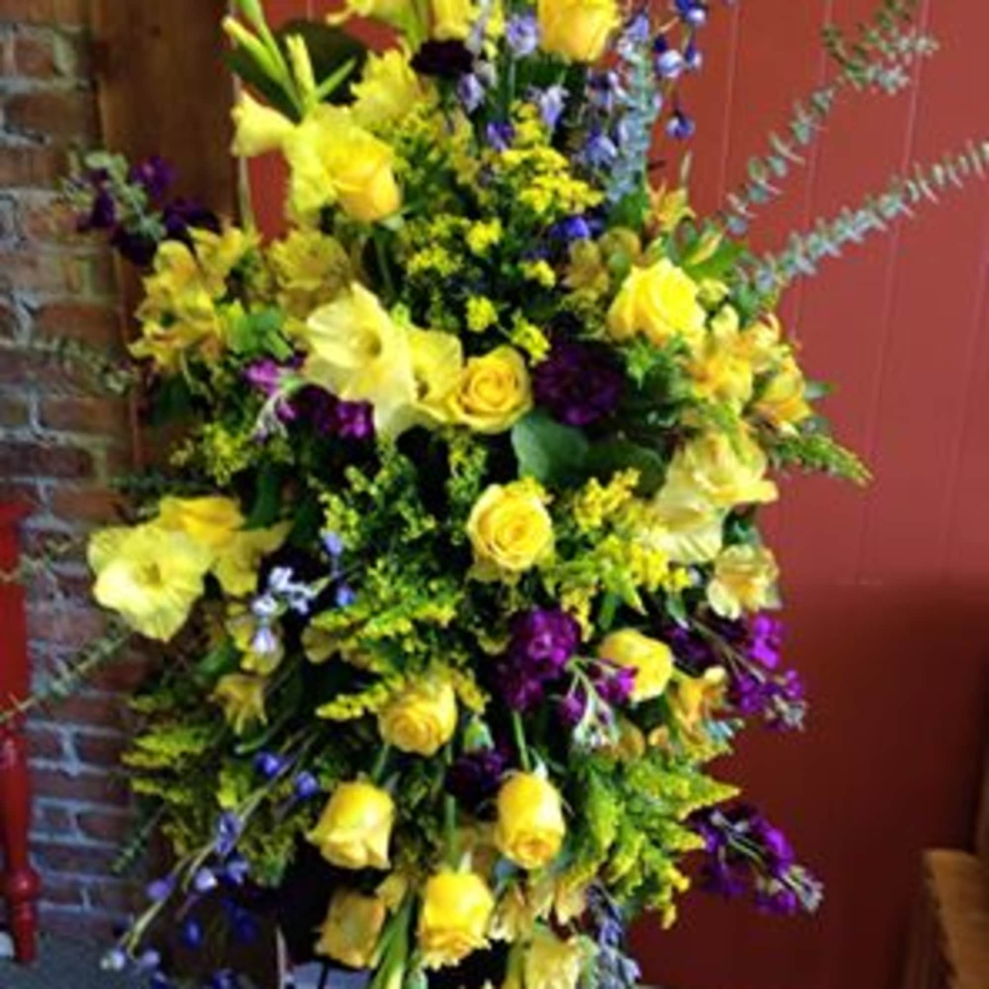 Tall floral spray with yellow roses and lilies accented by purple flowers