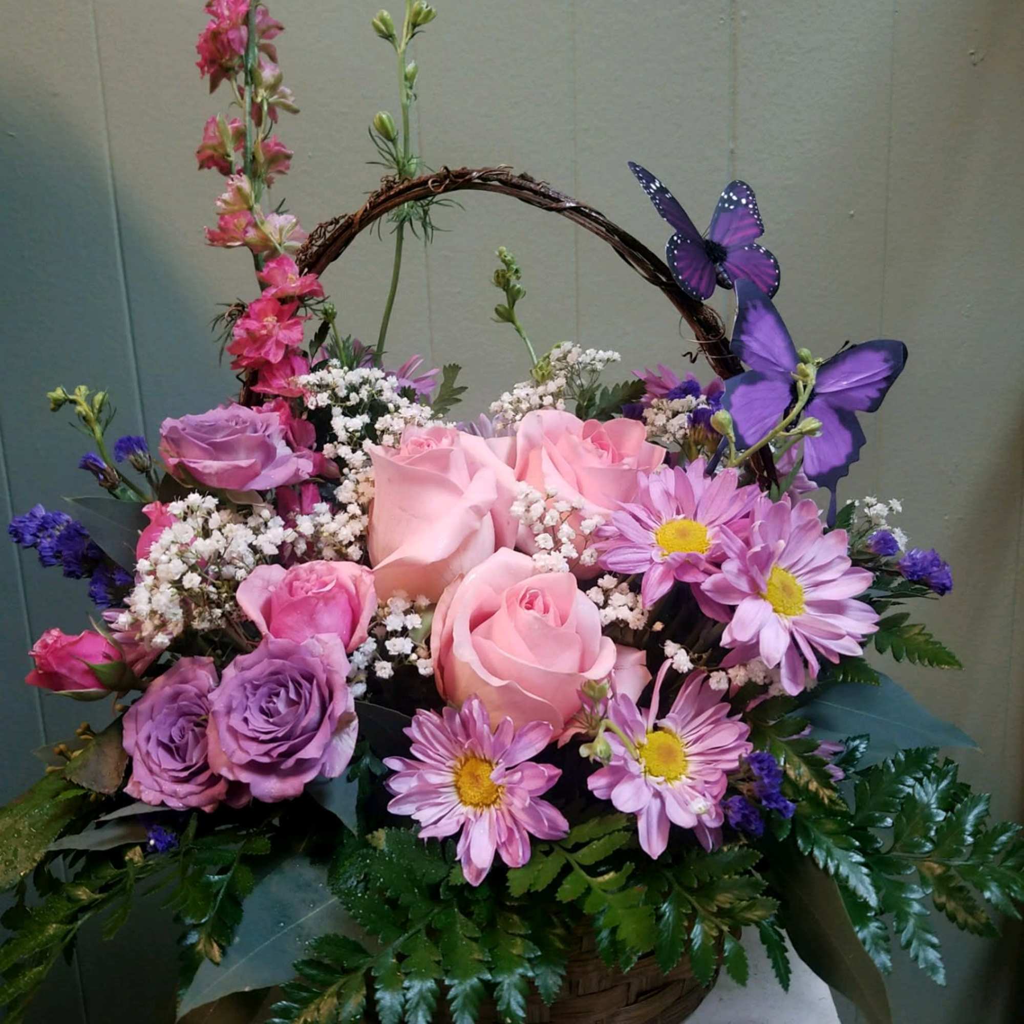 Basket arrangement of pink and purple roses with daisies and butterflies