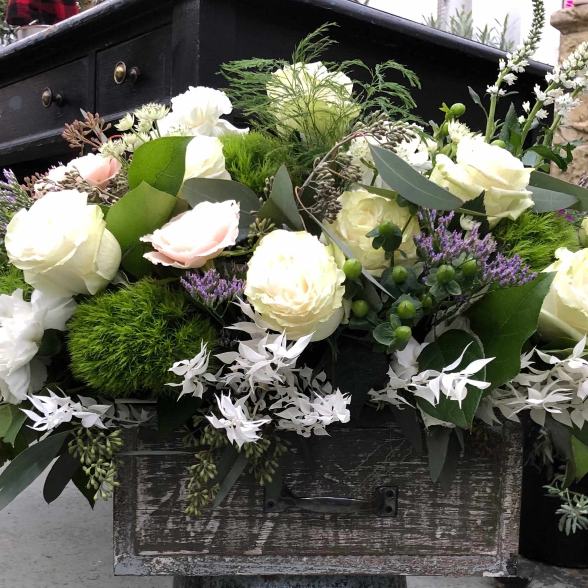 White and pale pink roses arranged with greenery in a rustic container