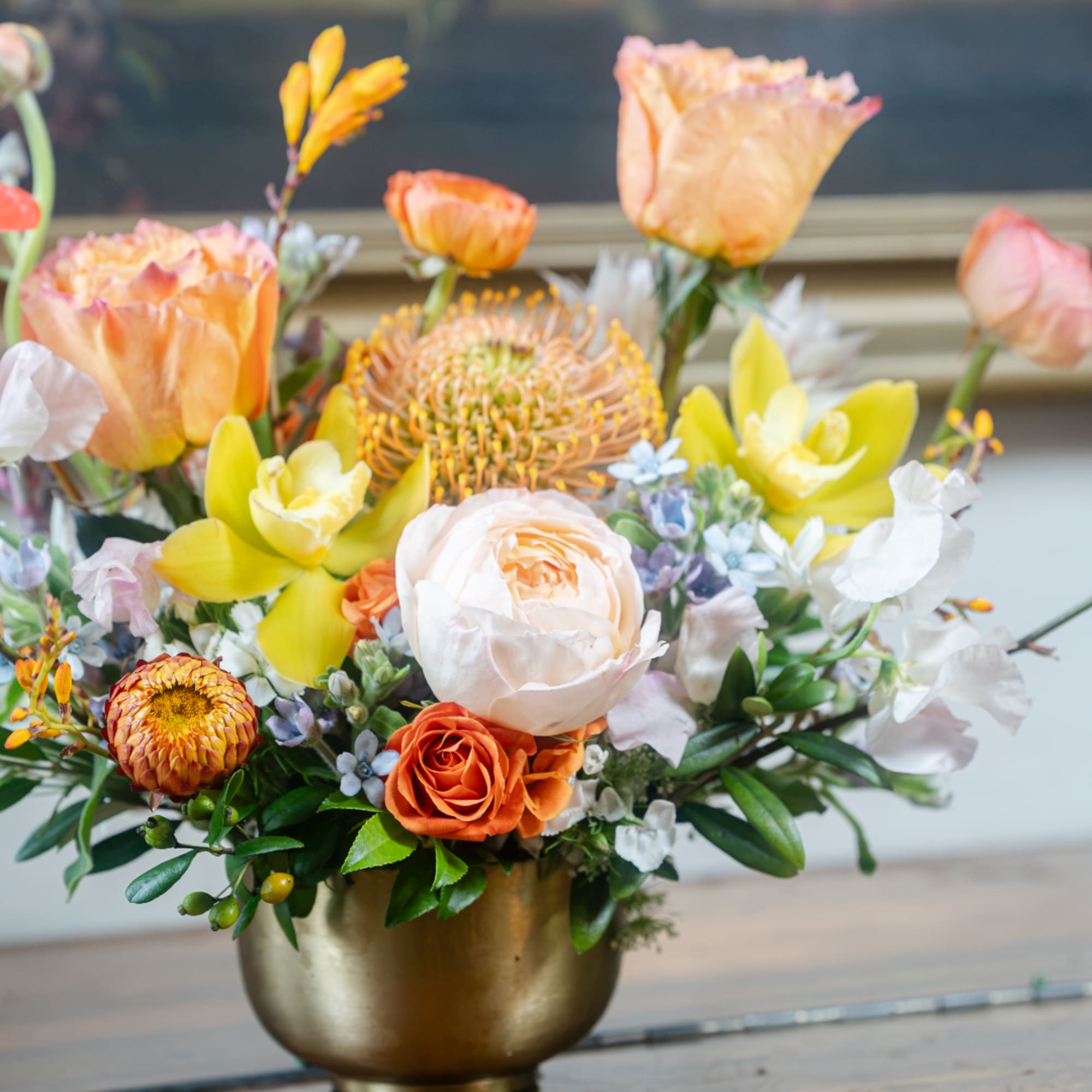 Mixed floral arrangement in a gold vase with peach, yellow, white, and orange blooms