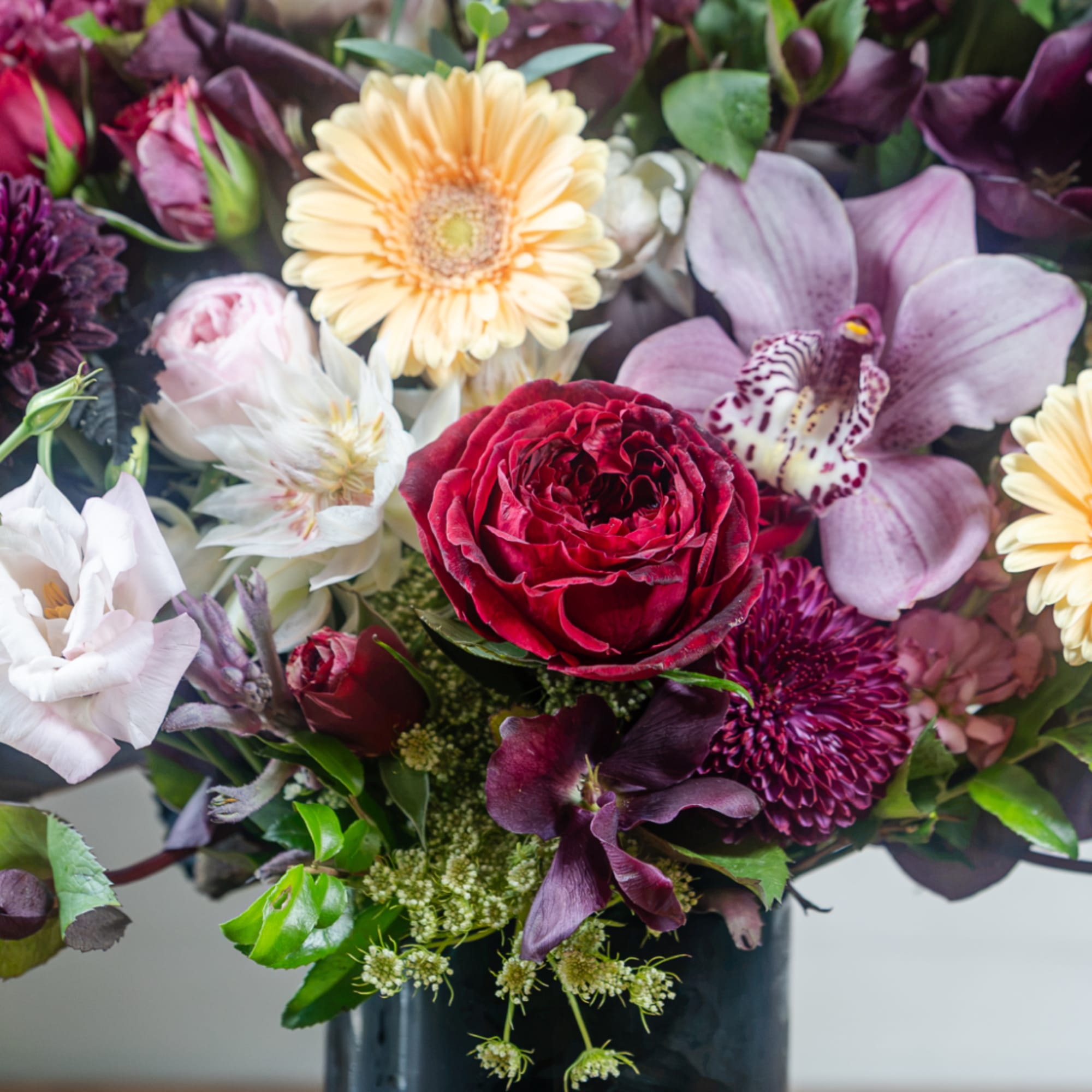 Mixed bouquet with red rose, pale gerbera daisies, and purple orchids in a dark vase
