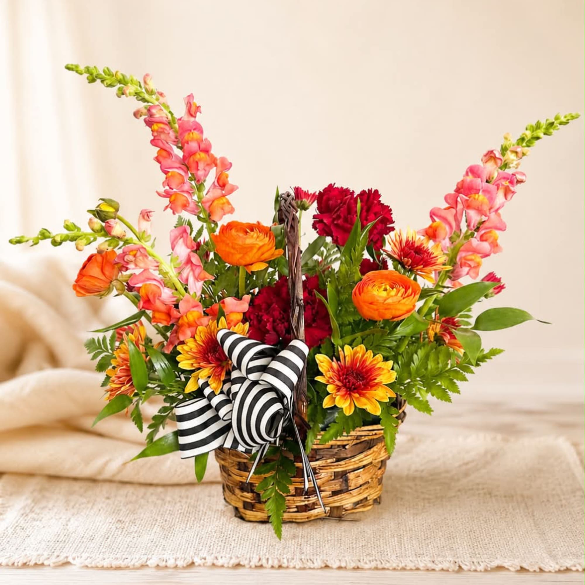 Basket arrangement of orange, pink, and red flowers with a striped ribbon