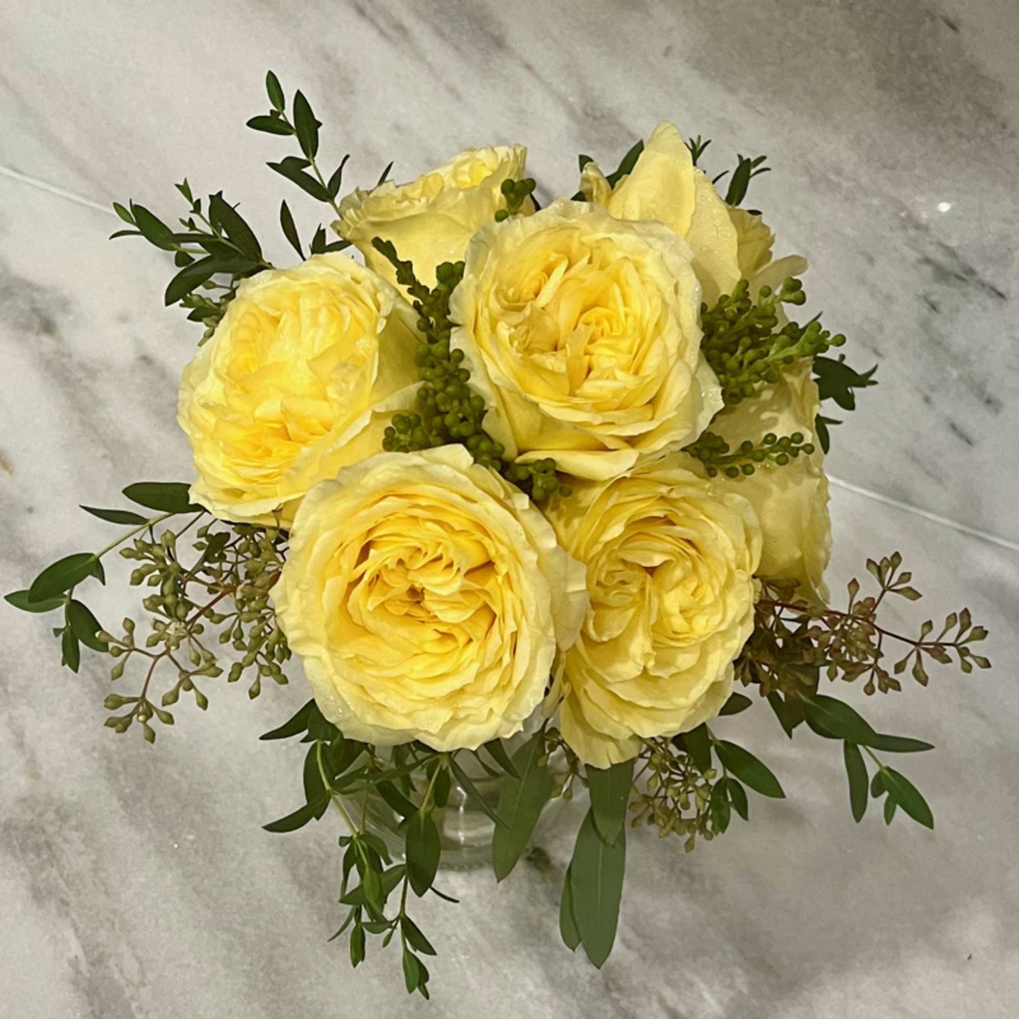 Yellow rose bouquet in a clear glass vase with green filler