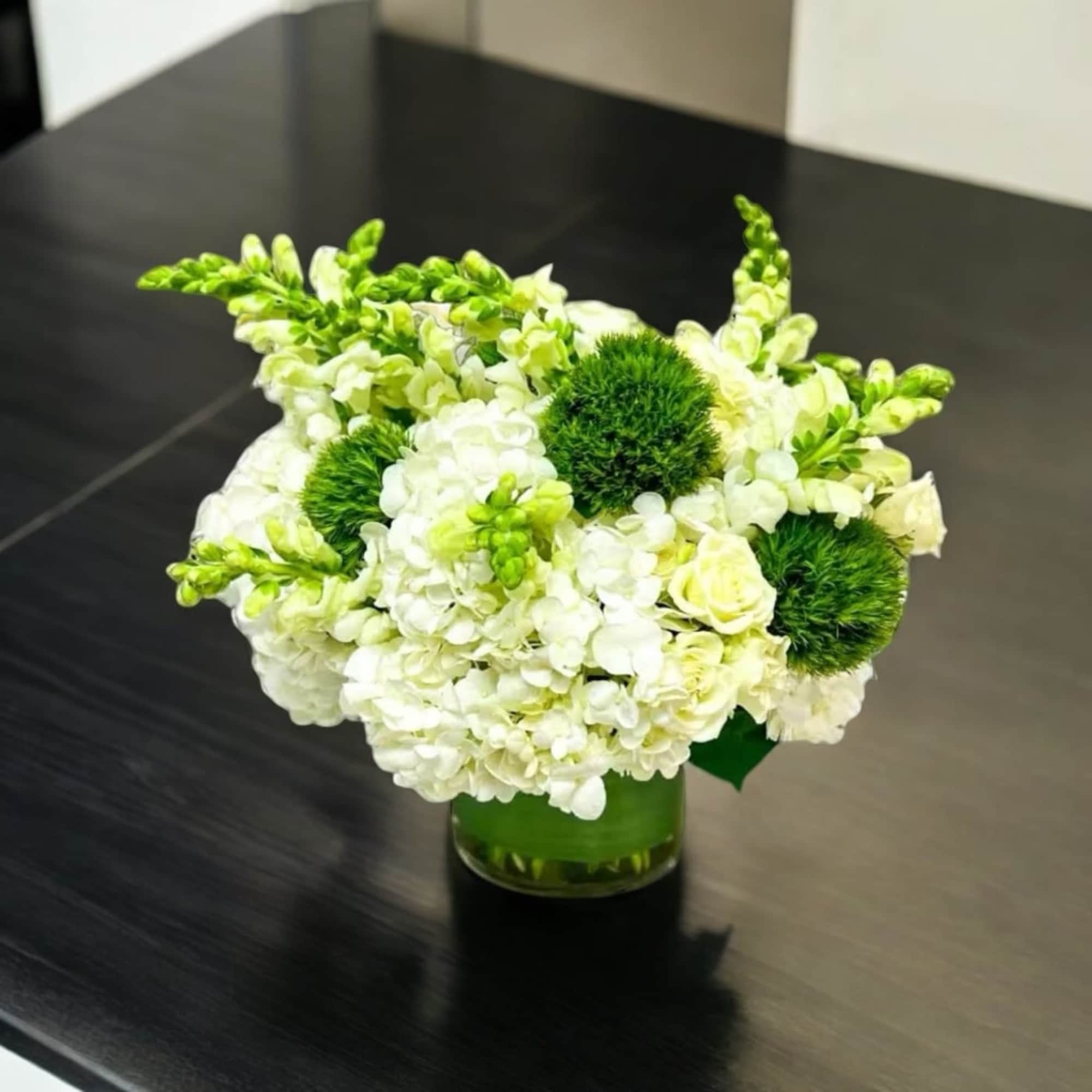 Cylinder vase displaying hydrangeas, snap, dragons, spray roses and green dianthus balls.