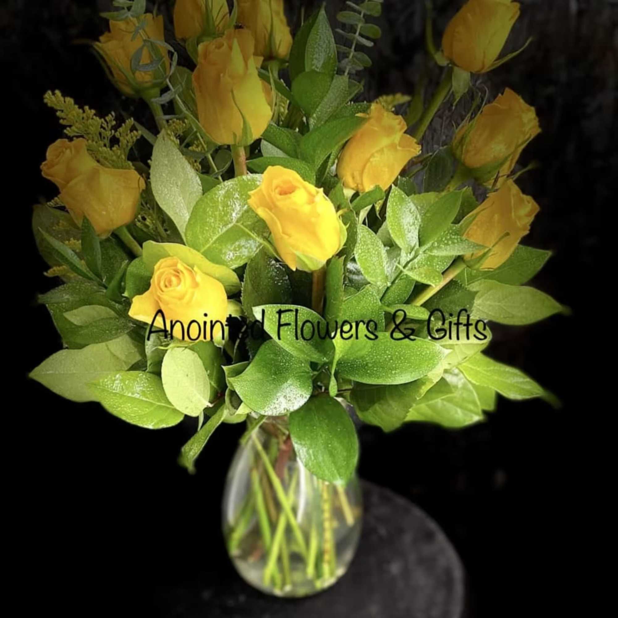 Arrangement of yellow roses in a clear glass vase against a dark background