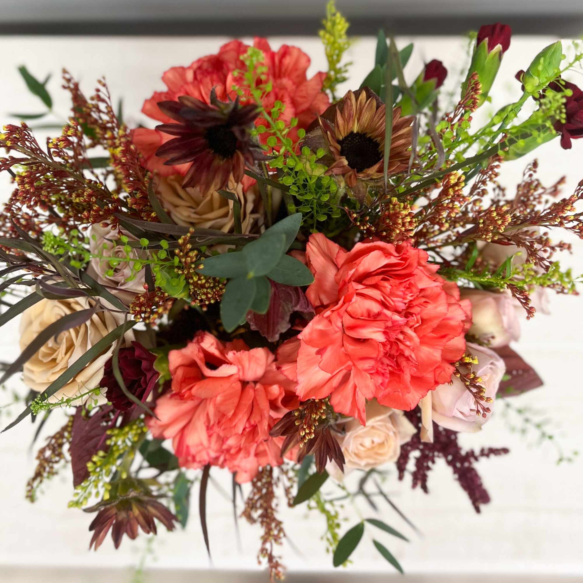 Bouquet of coral and burgundy flowers with mixed greenery