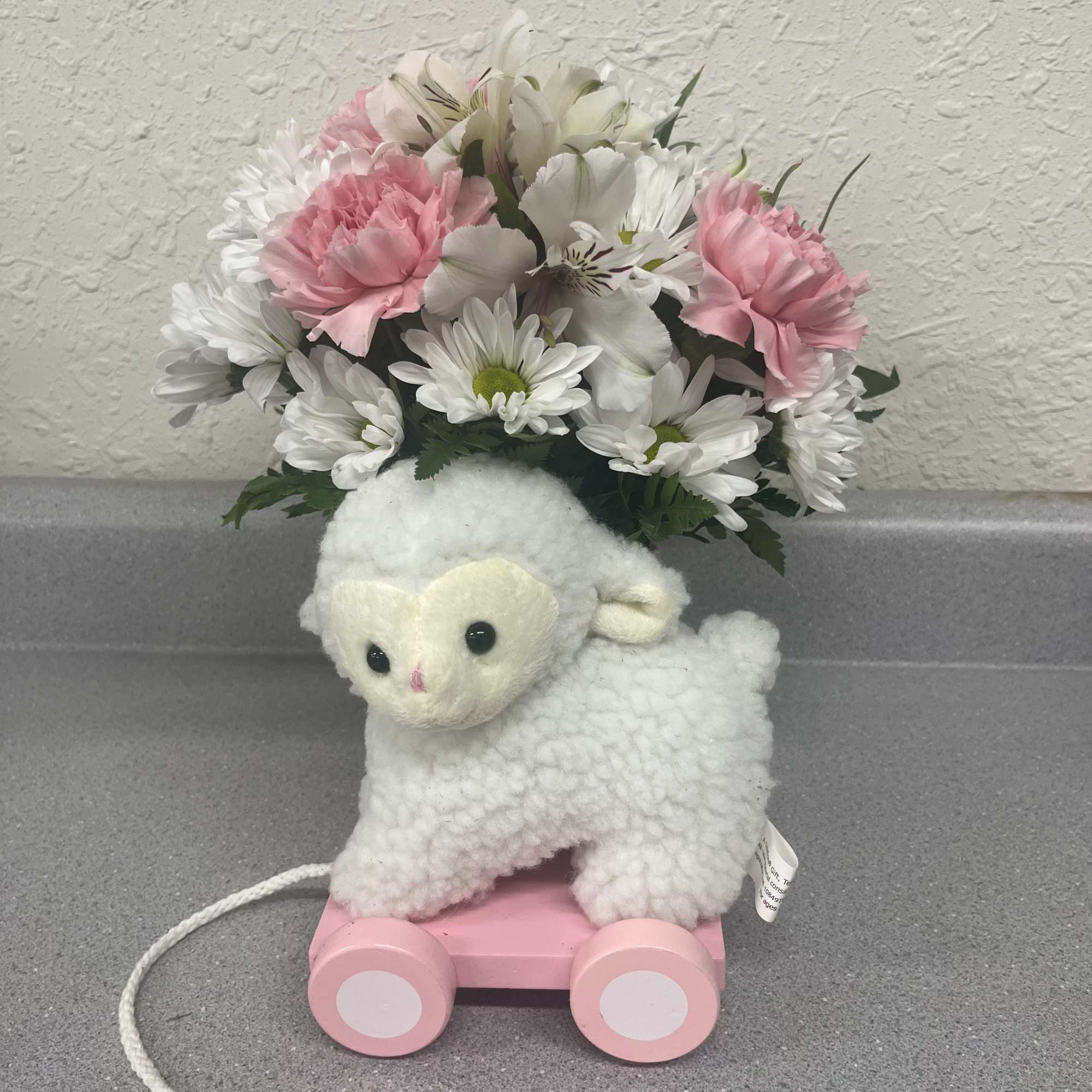 Plush lamb toy with a pink wheeled base and a bouquet of pink and white flowers