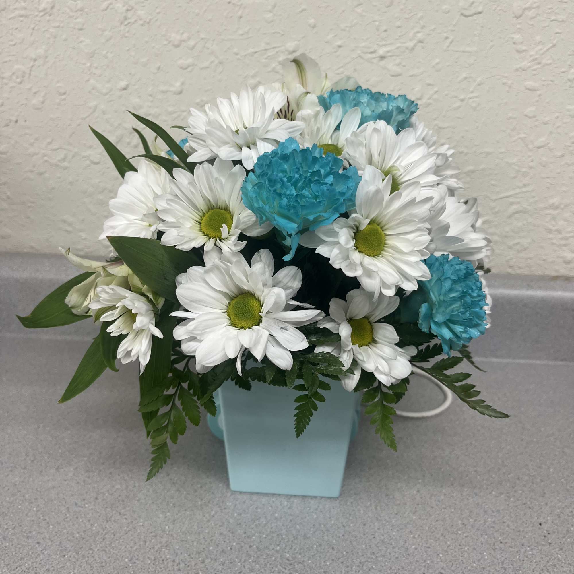 White daisies and blue carnations in a light blue vase