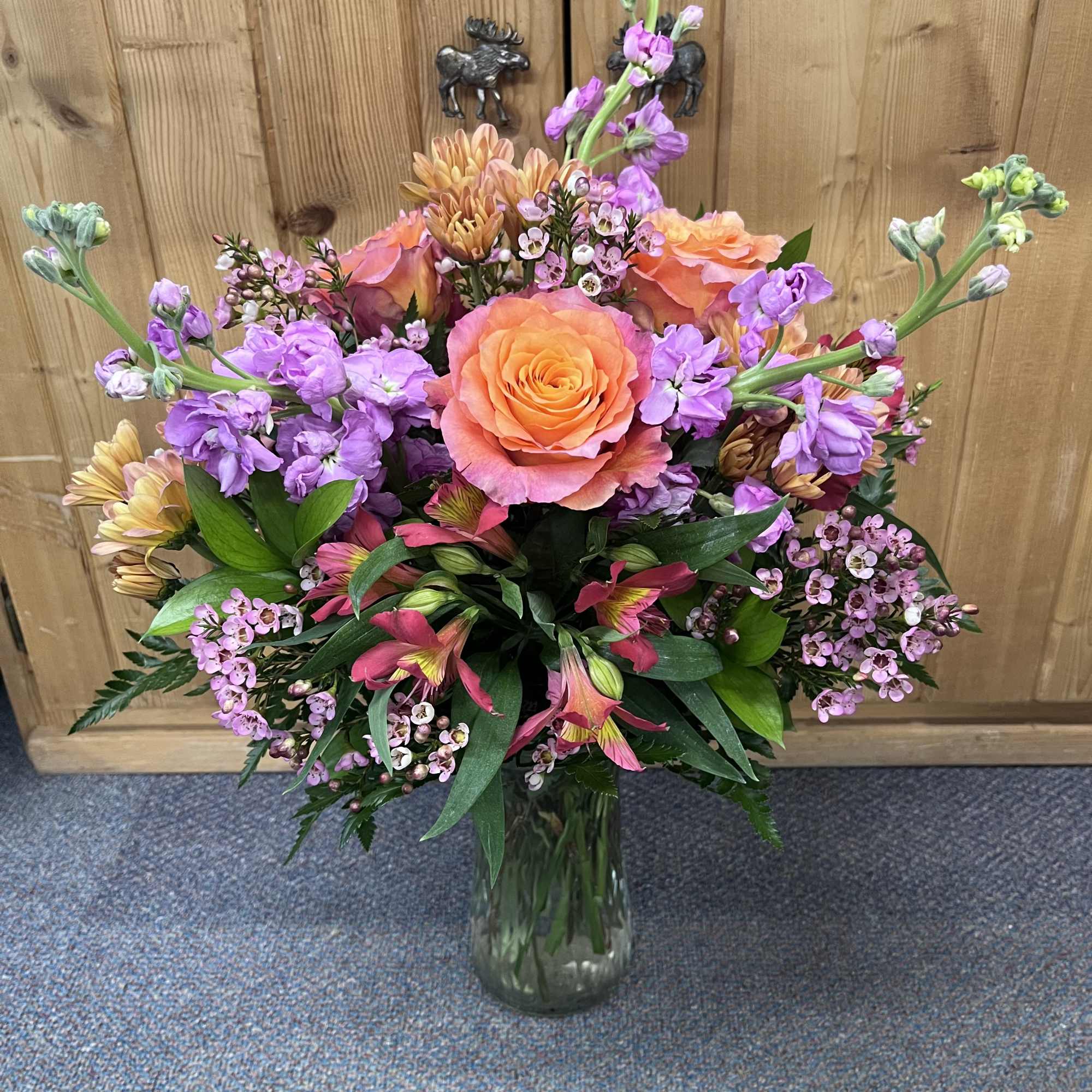 Mixed bouquet of orange roses and purple flowers in a glass vase