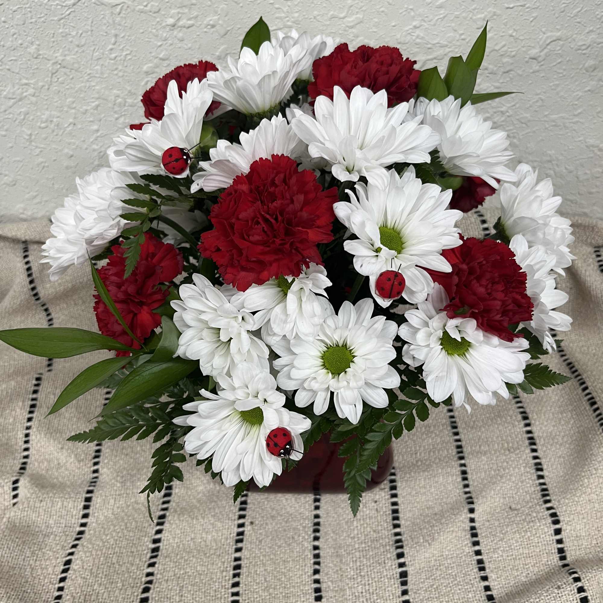 Red carnations and white daisies in a low arrangement with ladybug picks
