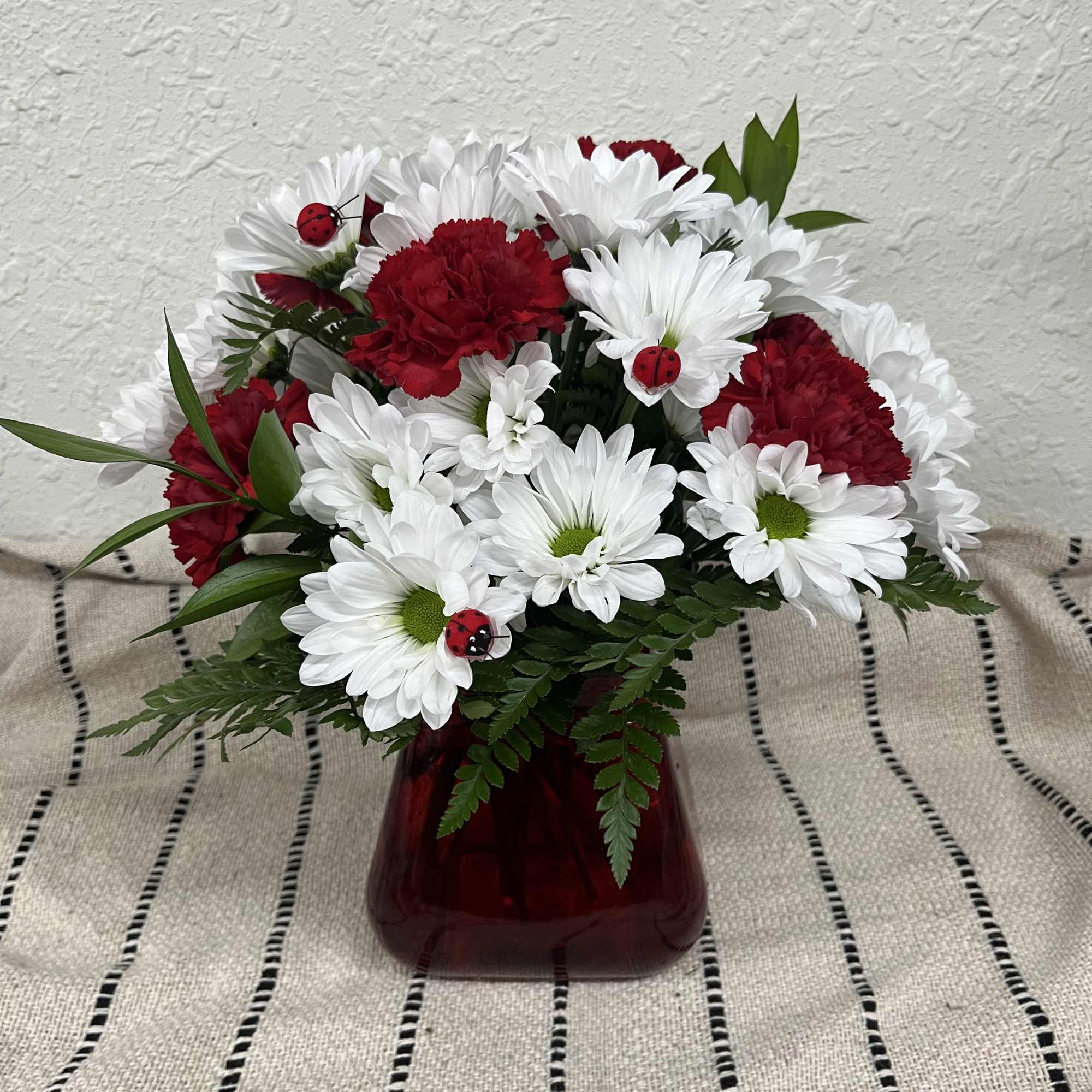 Red carnations and white daisies in a red vase with small ladybug decorations