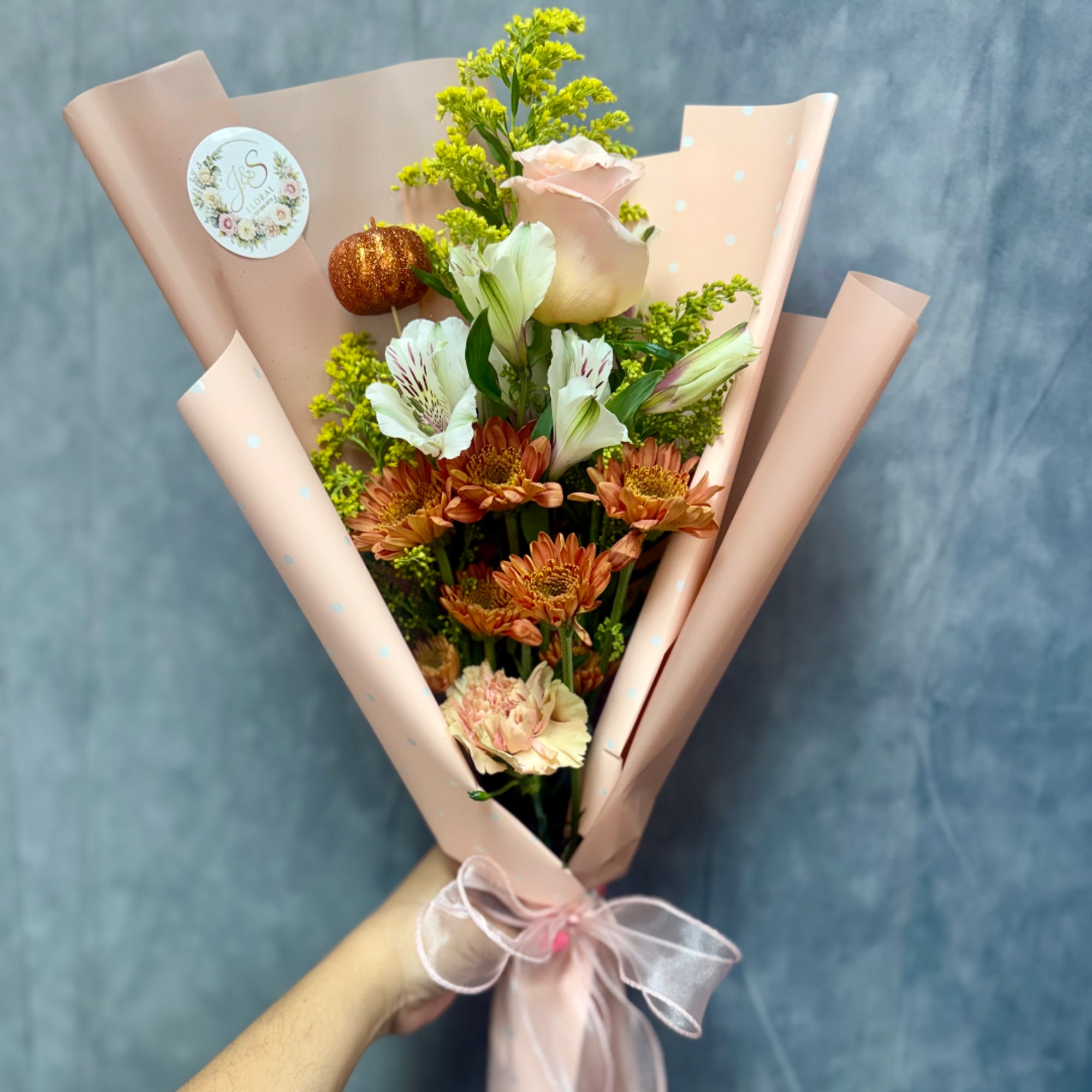 Handheld bouquet of peach and white flowers wrapped in pink paper