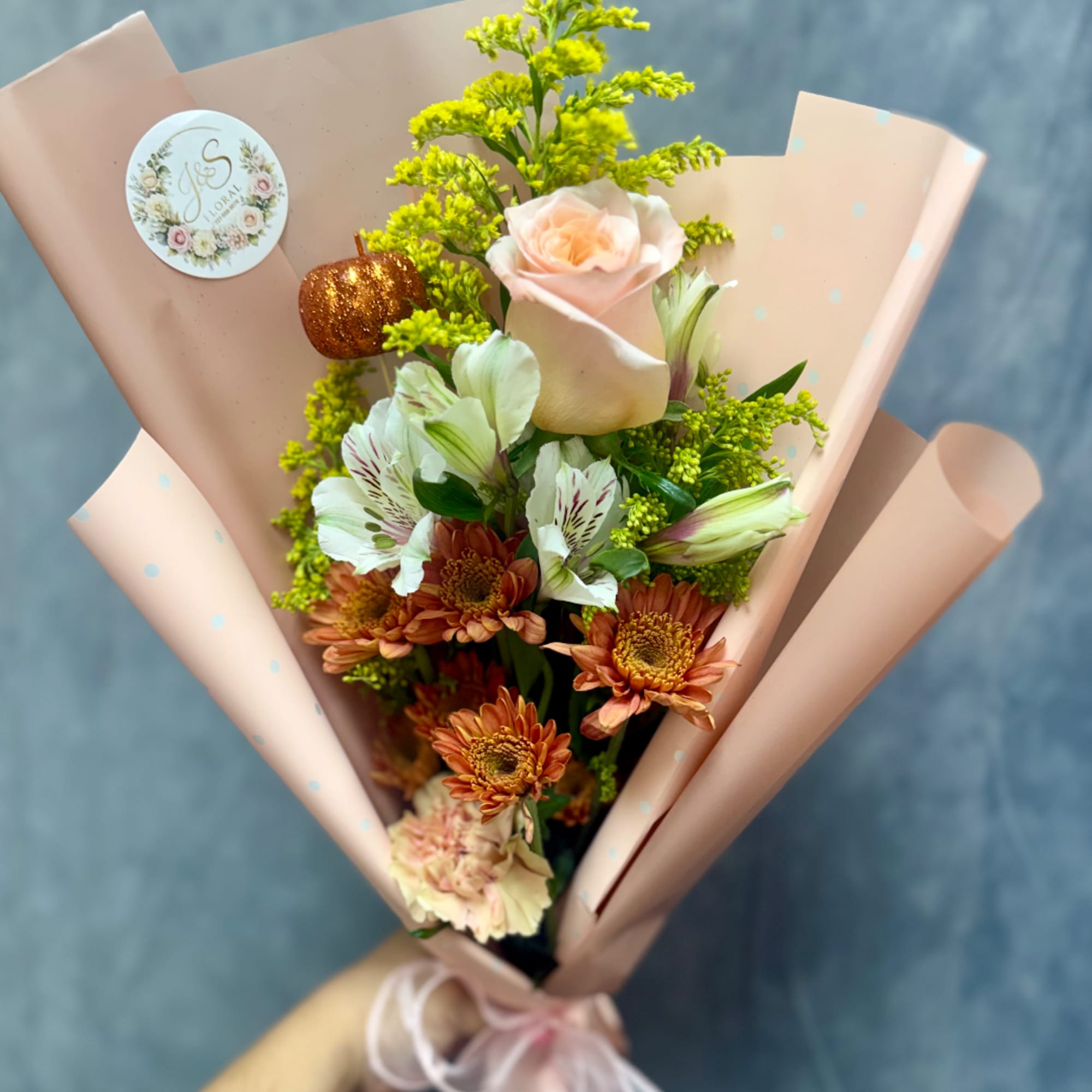 Bouquet of peach roses, white alstroemeria, and orange chrysanthemums in pink wrap