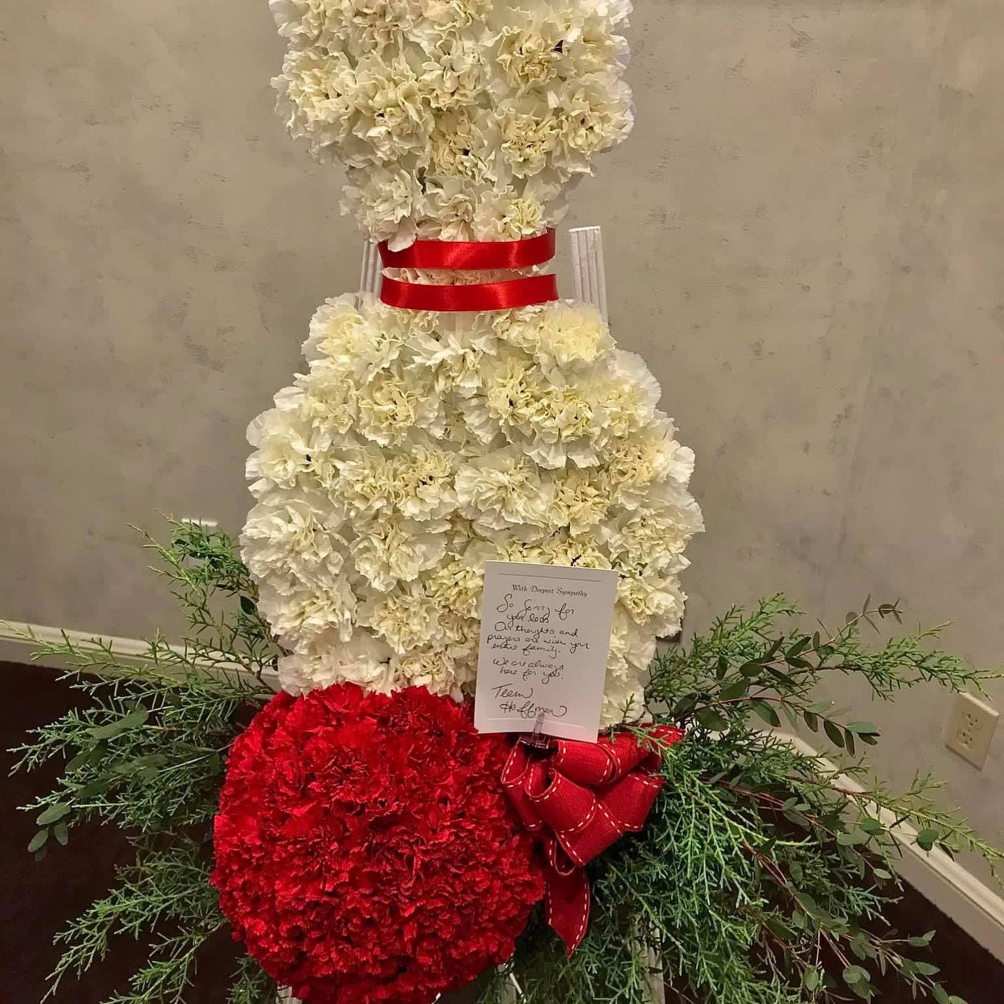 Standing floral spray shaped like a white dog with a red round base on an easel