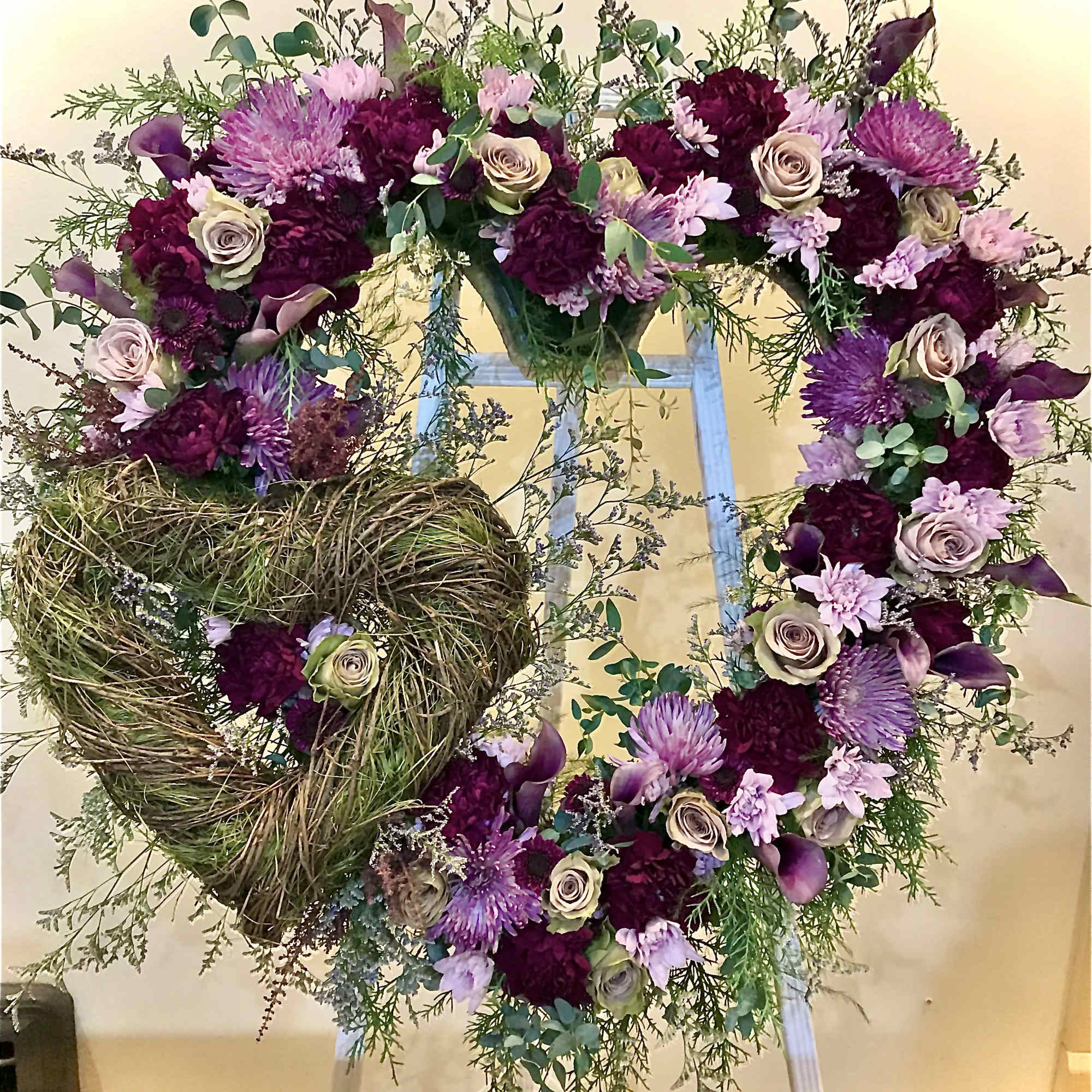 Heart-shaped standing wreath with purple and lavender flowers and twig heart accent on an easel.