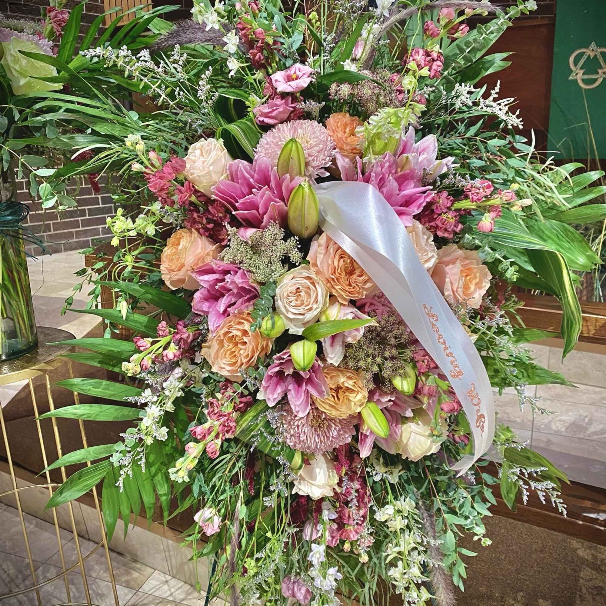 Tall standing spray of pink lilies and peach roses with a white ribbon on an easel