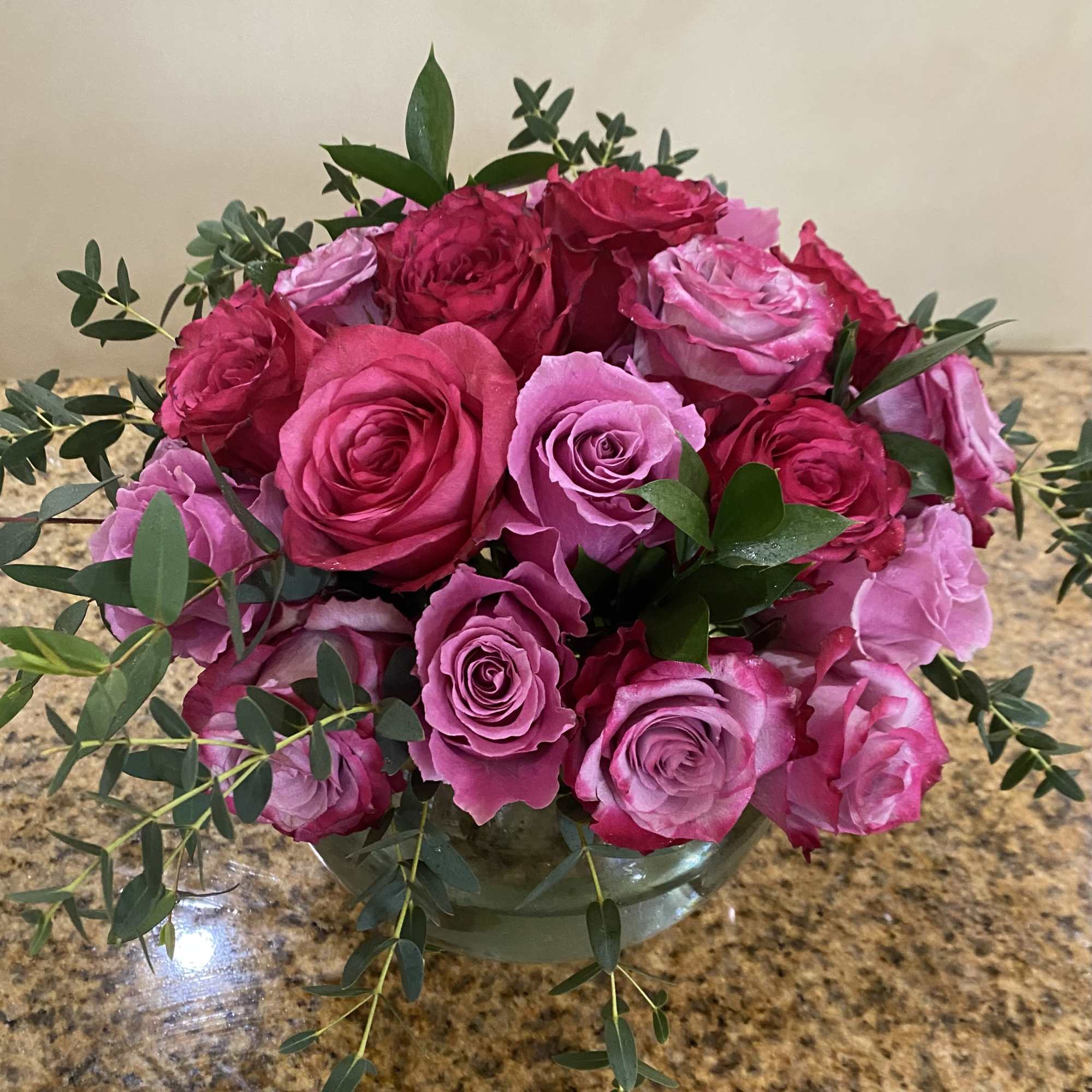 Low round arrangement of pink and fuchsia roses in a clear glass bowl vase
