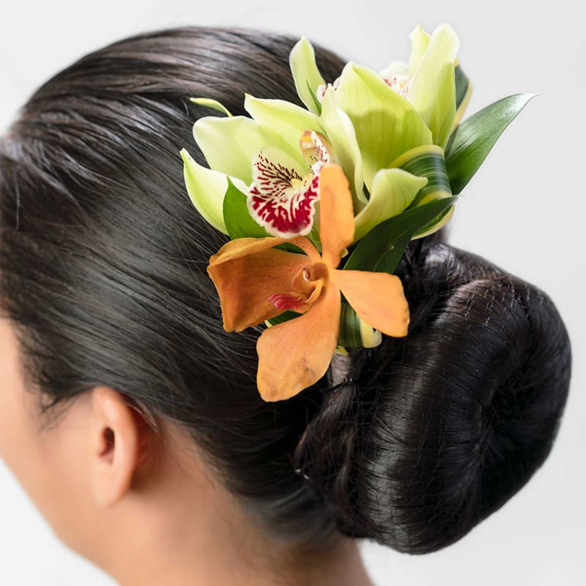 Orchid hairpiece with green and orange blooms pinned into a dark hair bun.