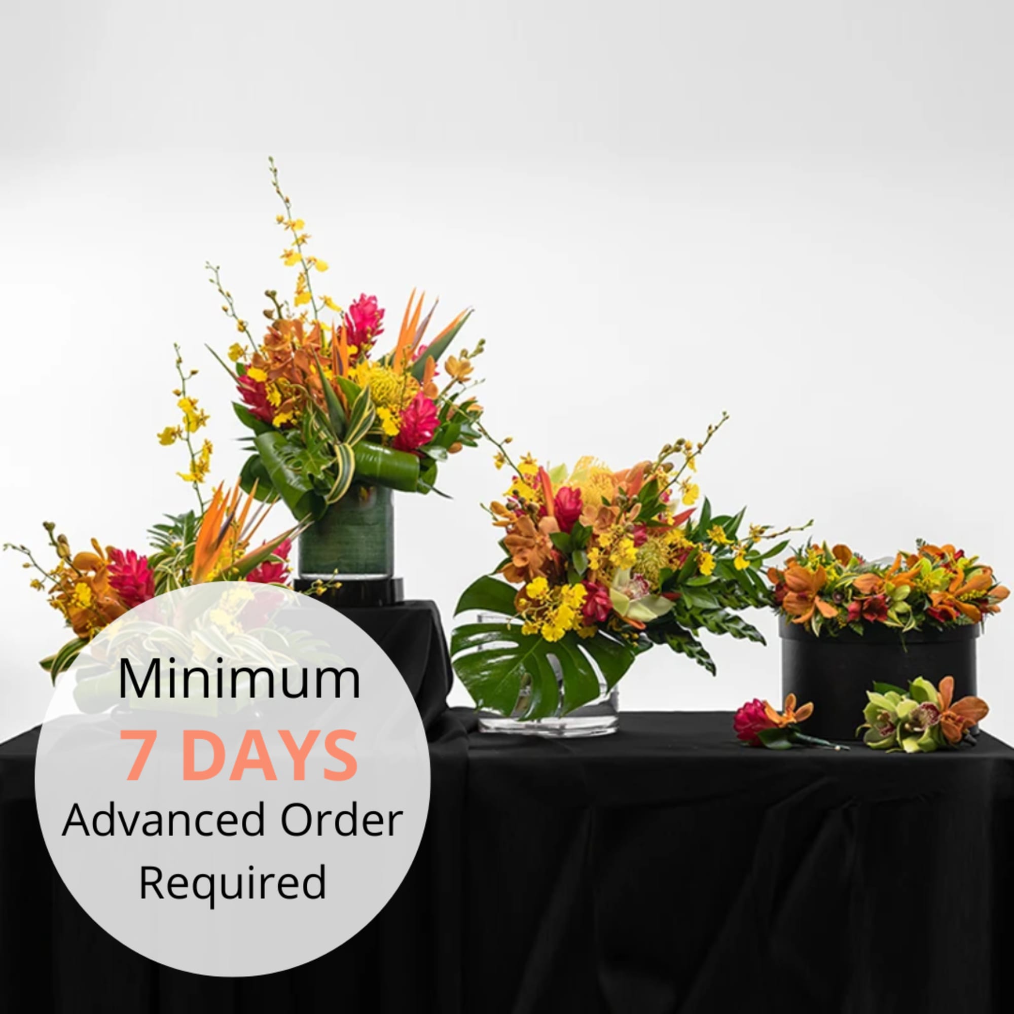 Set of colorful tropical floral arrangements in modern vases on a black-draped table.