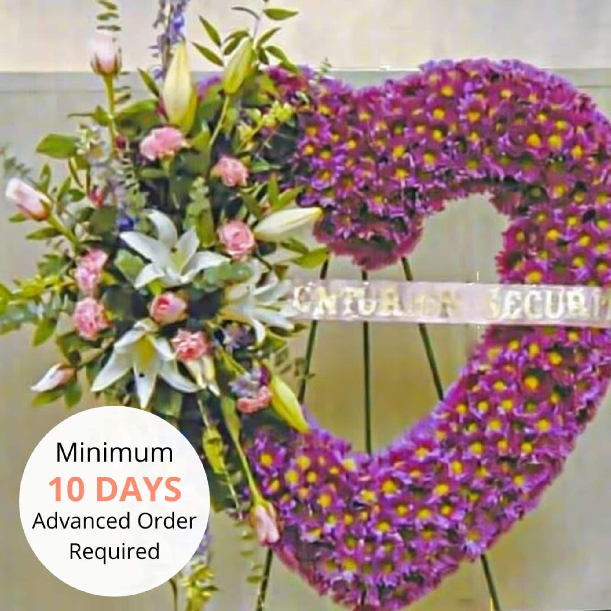 Heart-shaped purple standing wreath with white lilies and pink roses on an easel.