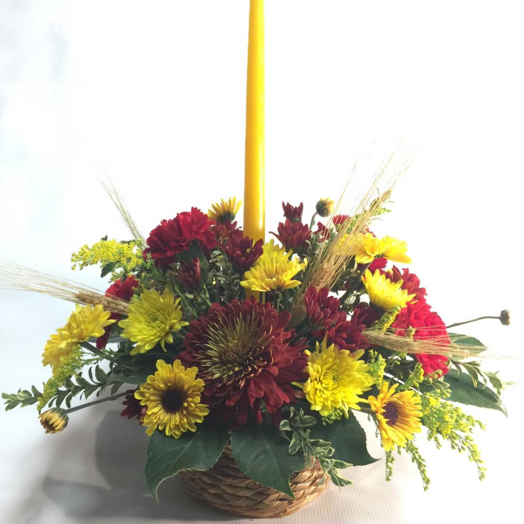 Basket arrangement of yellow and red flowers with a tall yellow candle