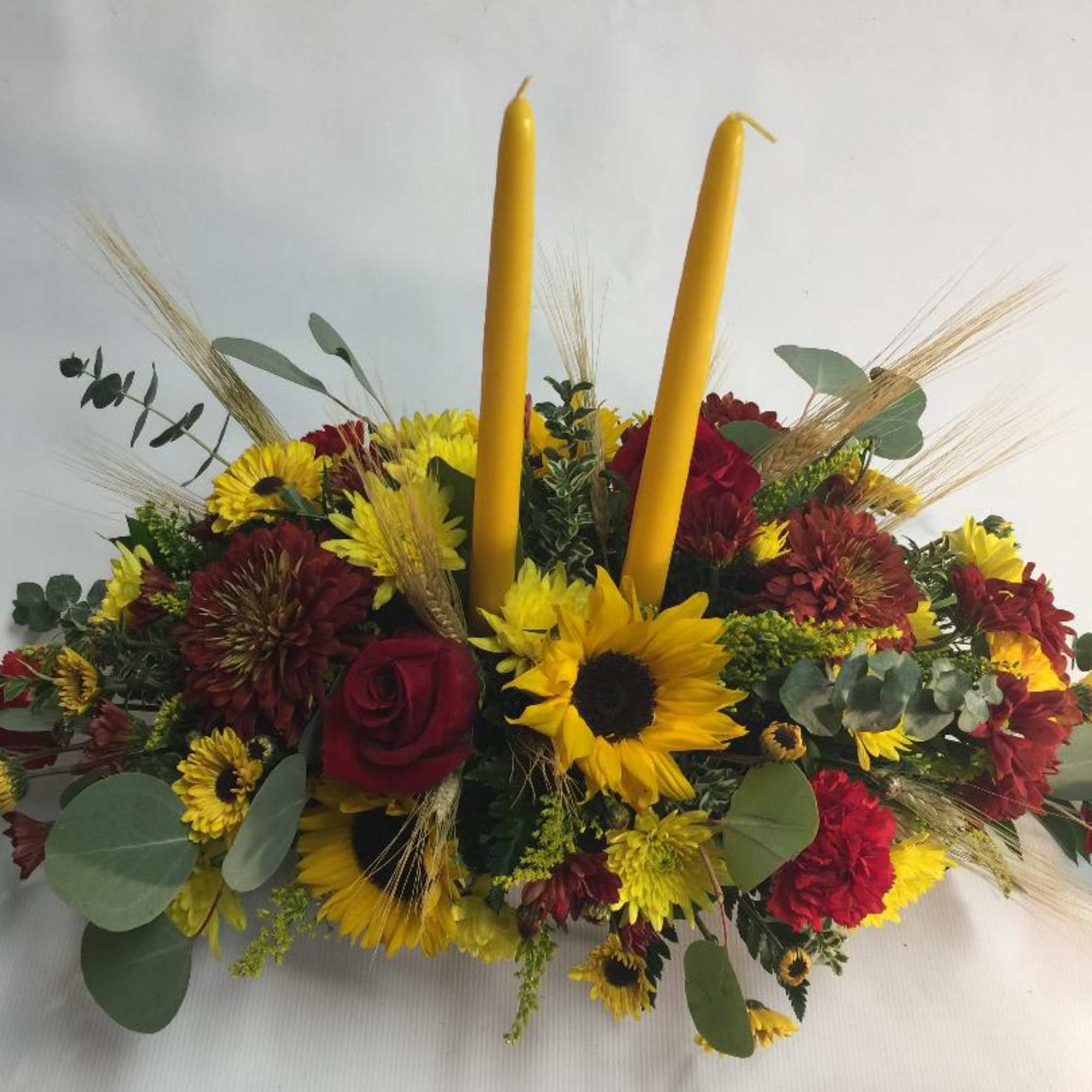 Low floral centerpiece with sunflowers, red roses, and two yellow candles