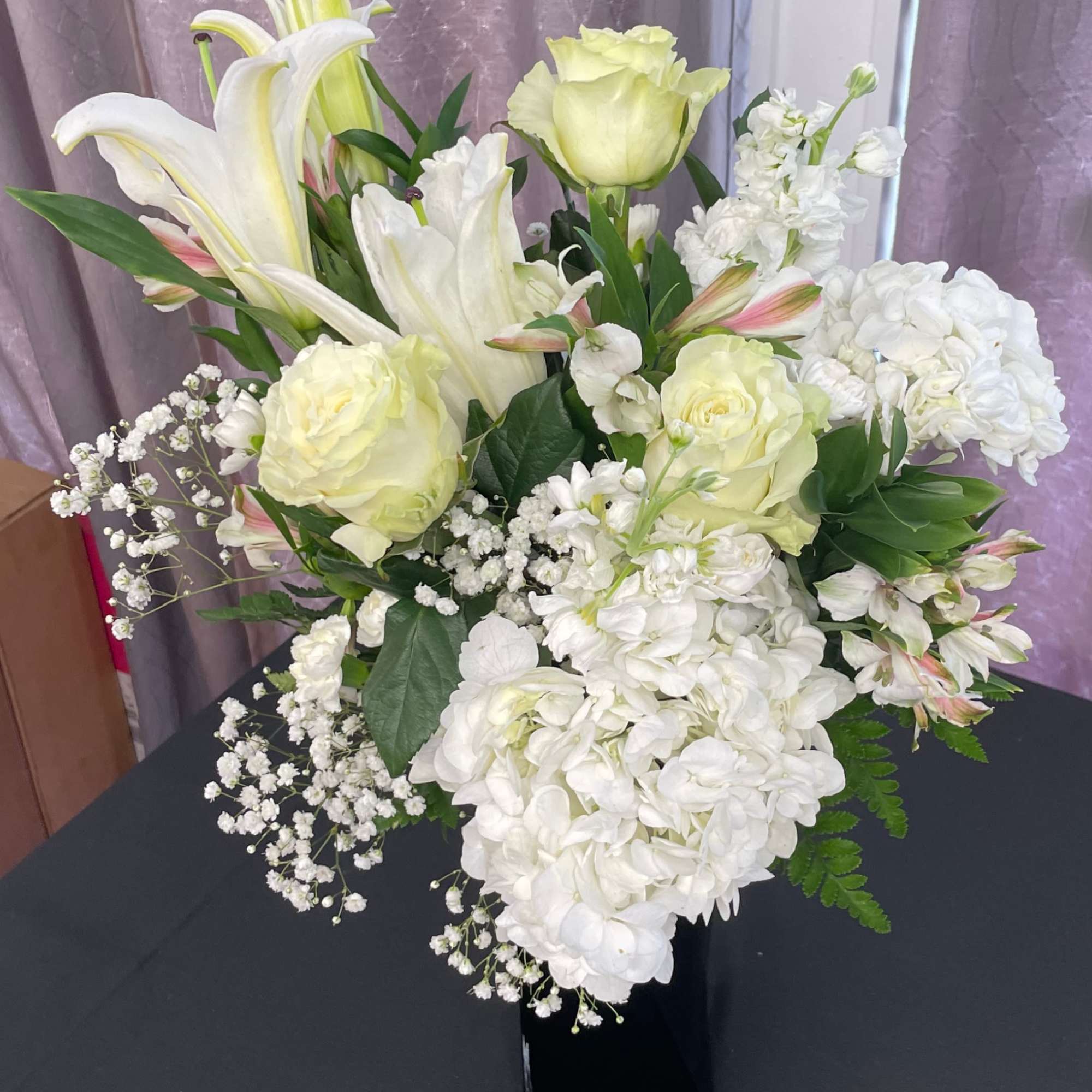 White lilies, roses, and hydrangeas arranged in a black vase