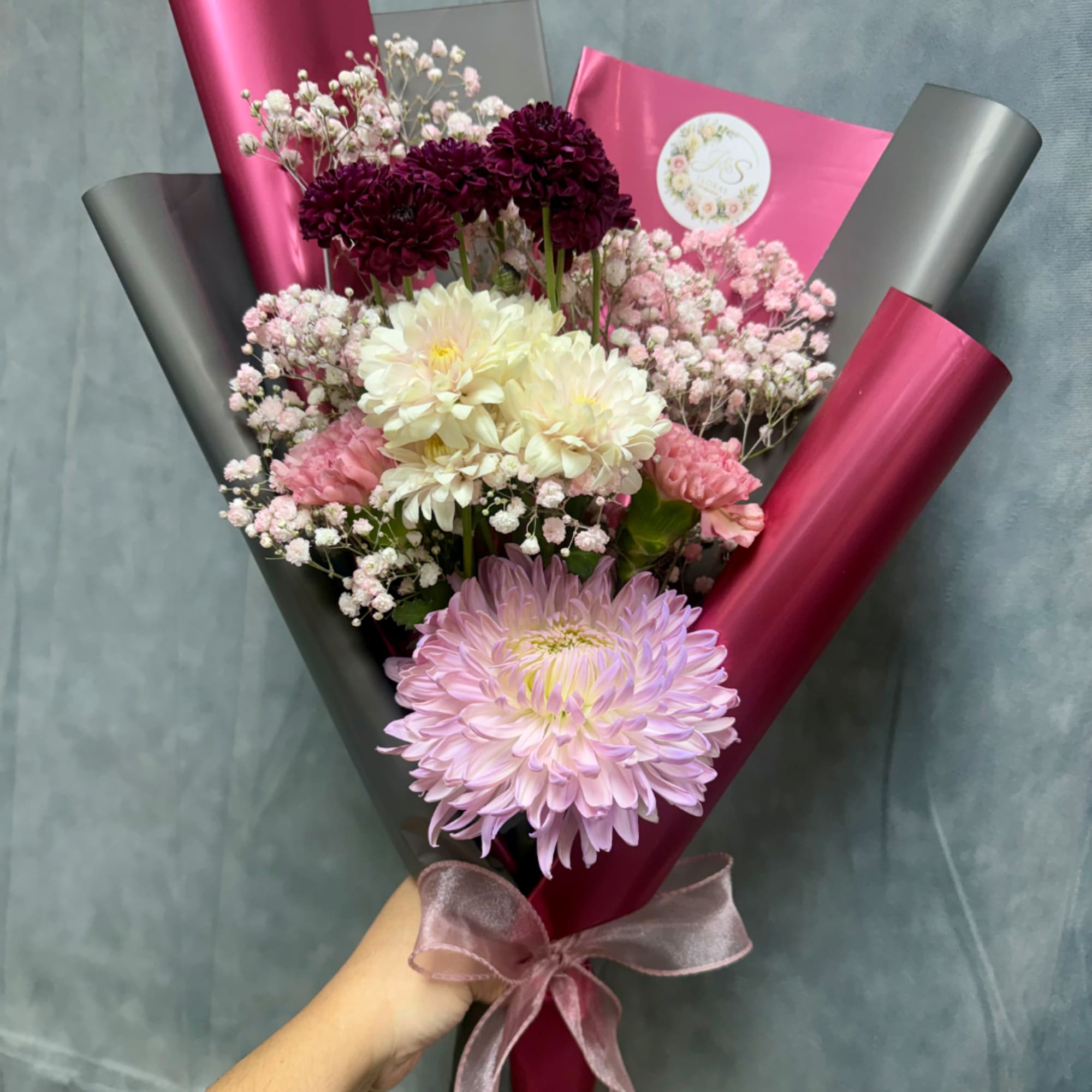 Handheld bouquet of pink, white, and burgundy flowers wrapped in magenta and black paper