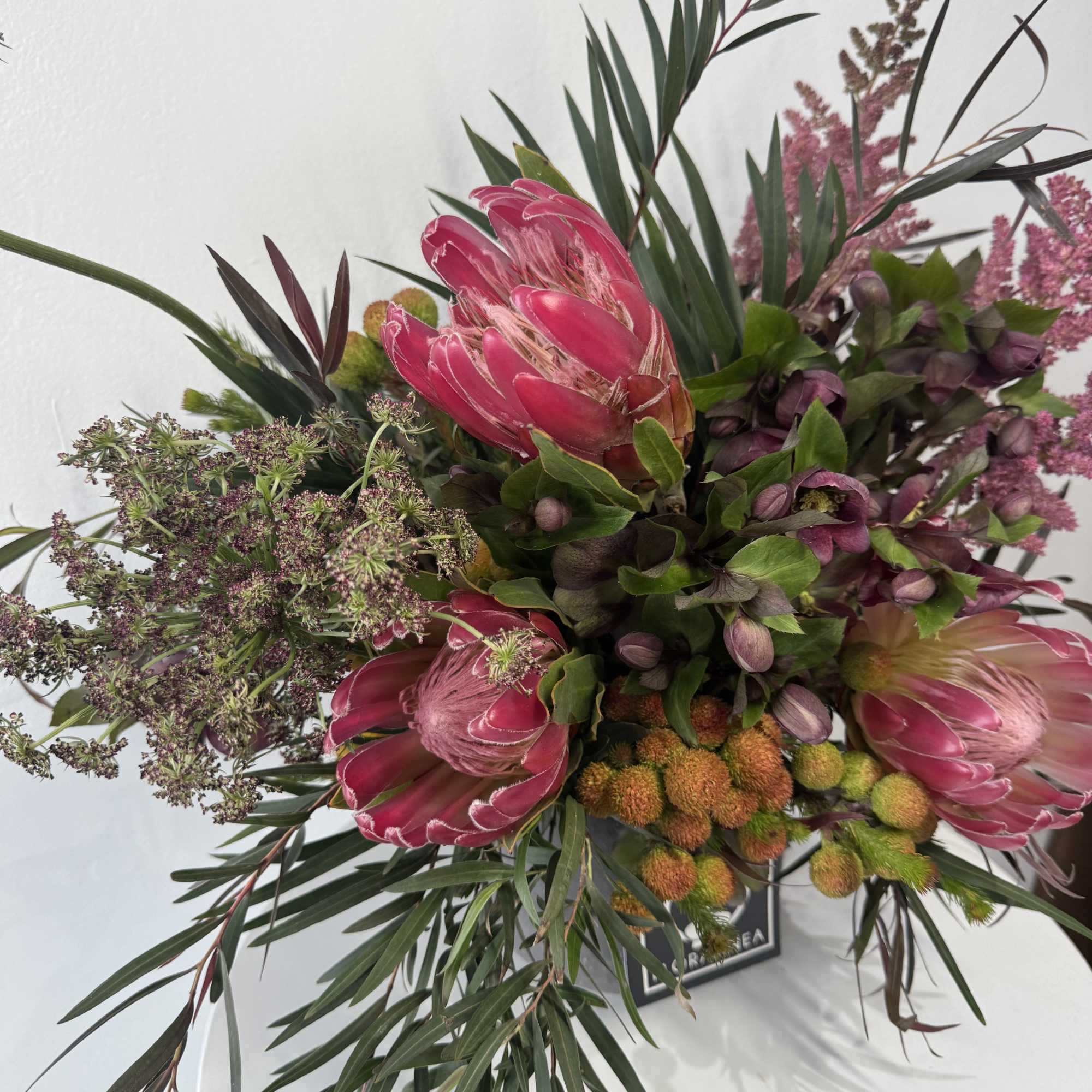 Bouquet of pink protea with dark foliage and small purple filler flowers