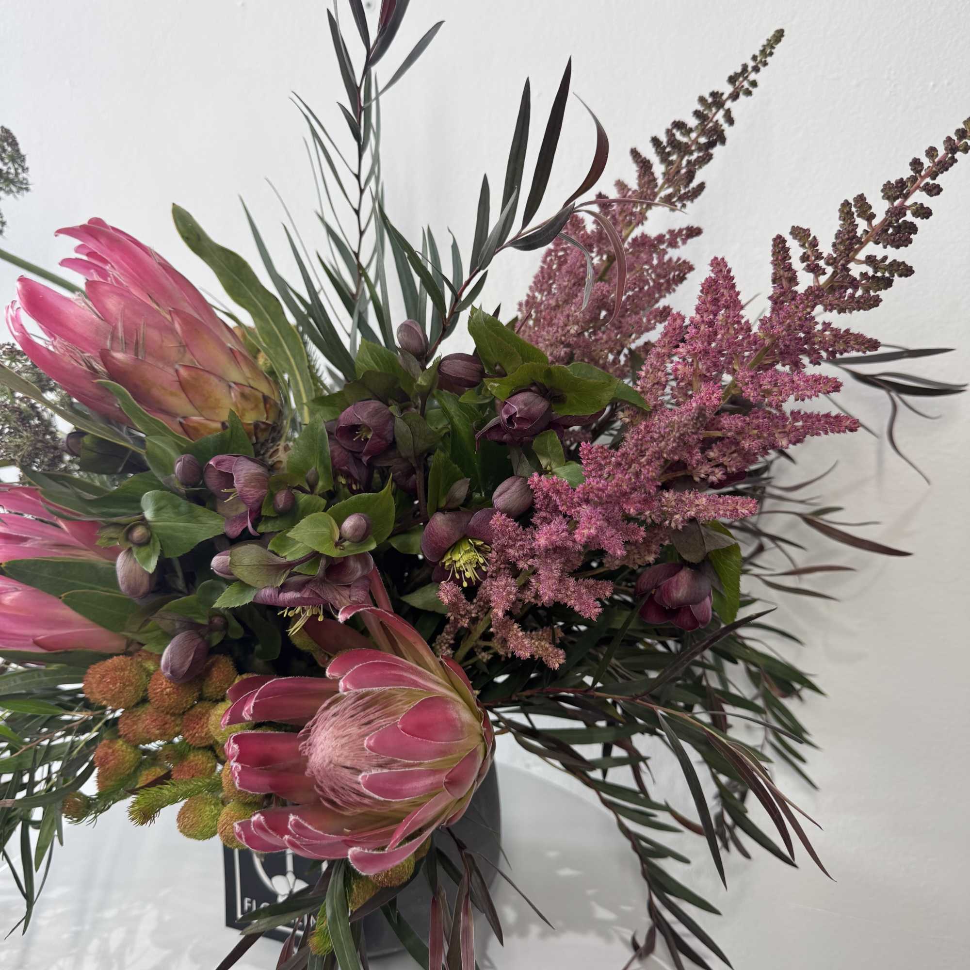 Pink protea bouquet with dark foliage in a black container