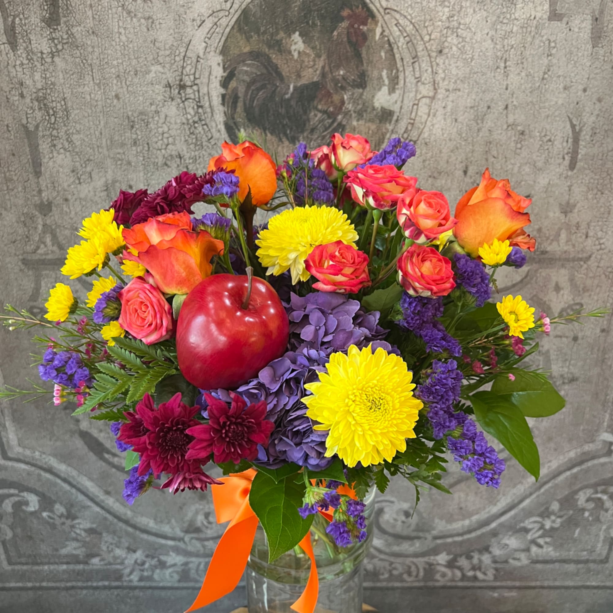 Colorful bouquet of roses, chrysanthemums, and hydrangeas in a glass vase with an apple