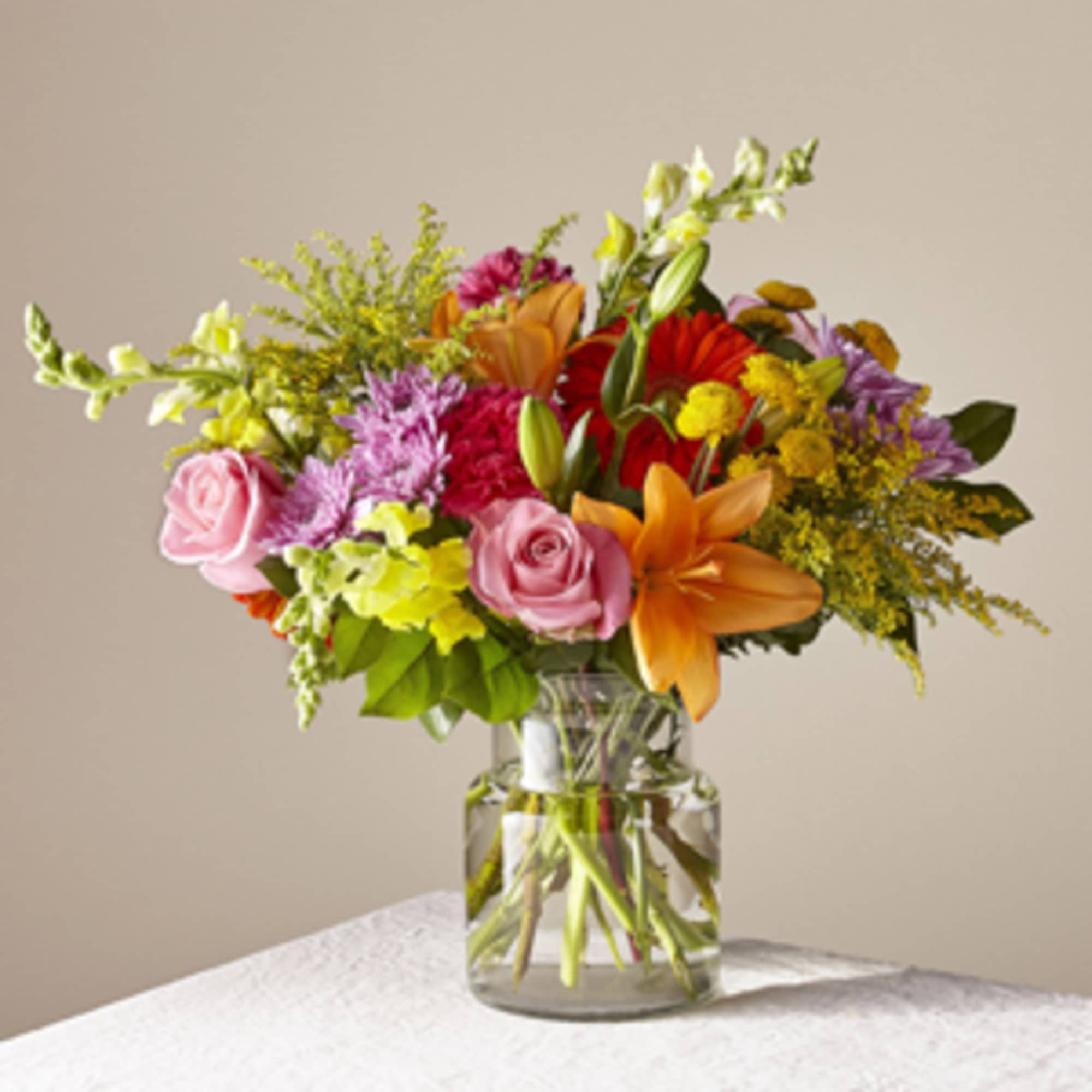 Mixed bouquet of roses, lilies, and daisies in a clear glass vase
