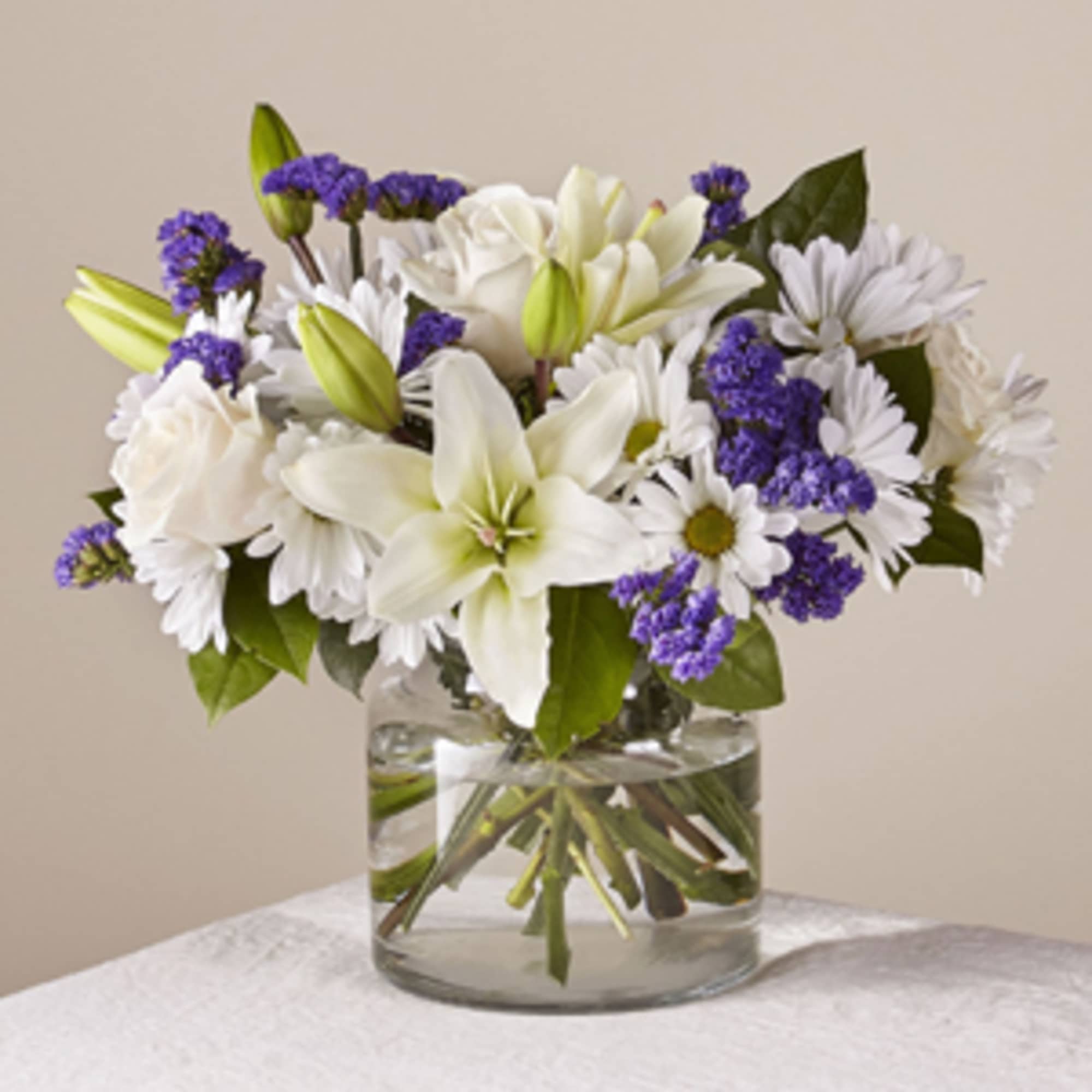 White lilies and daisies with purple filler in a glass vase