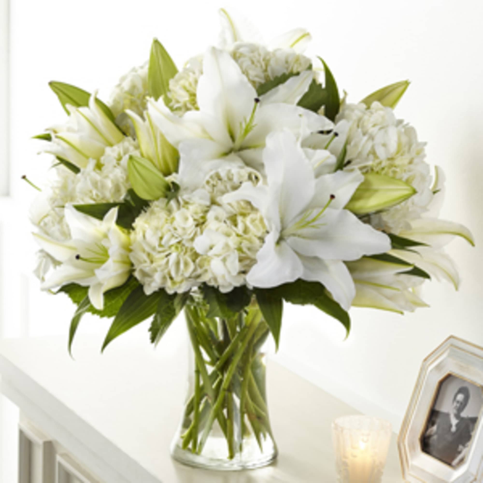 White lilies and hydrangeas arranged in a clear glass vase on a light table