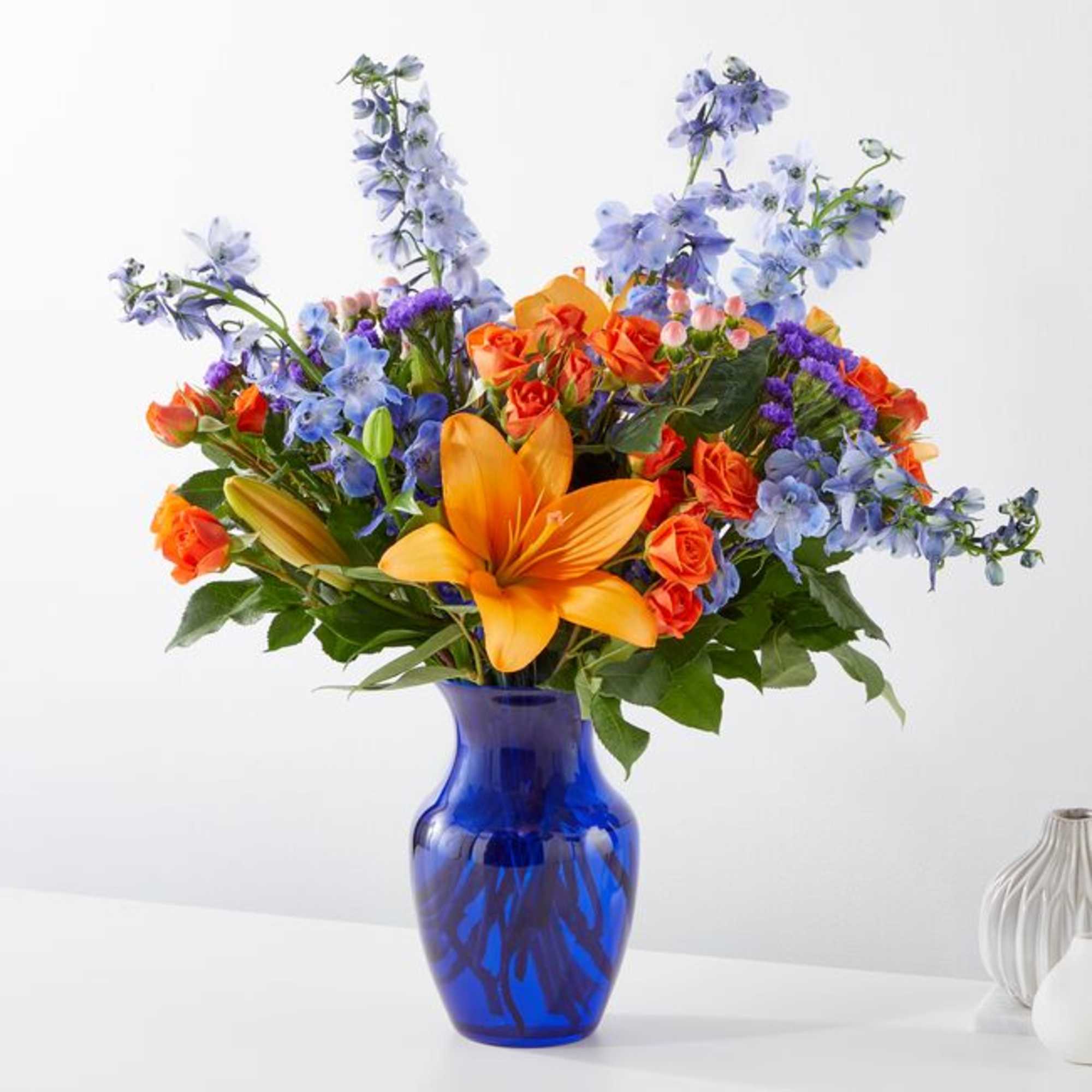 Colorful bouquet with orange lilies and blue flowers in a cobalt vase