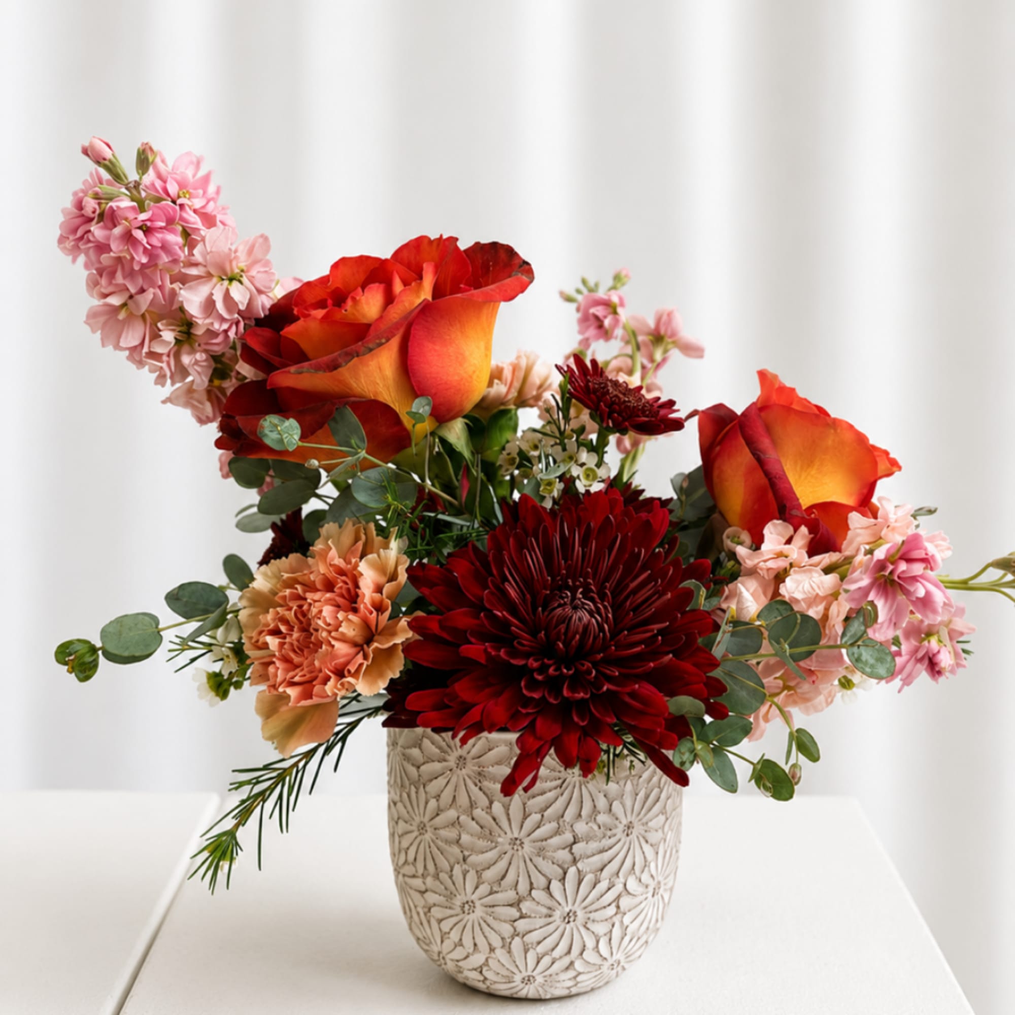 Mixed bouquet with orange-red roses and burgundy chrysanthemums in a patterned vase