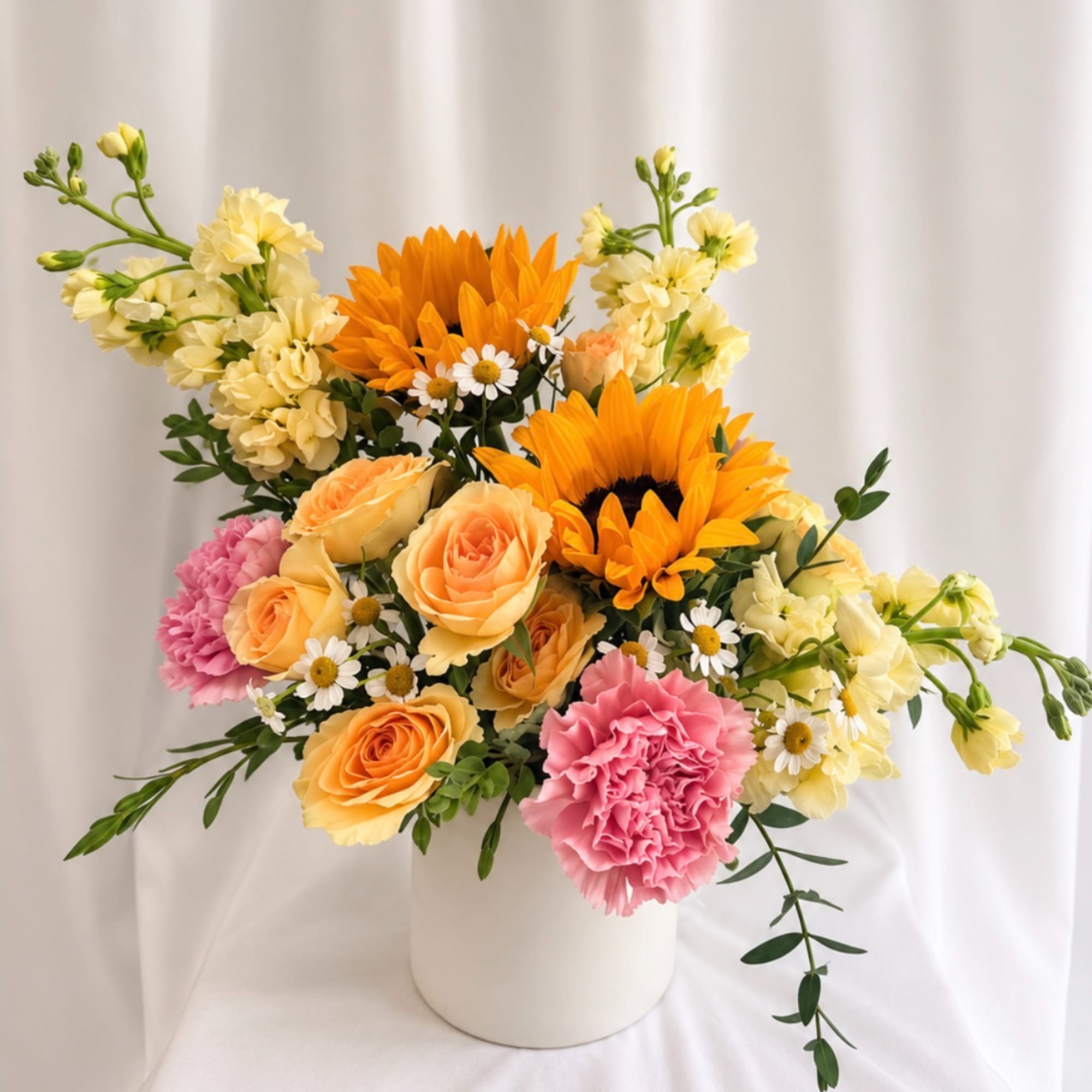 Mixed bouquet of sunflowers, roses, carnations, and small daisies in a white vase