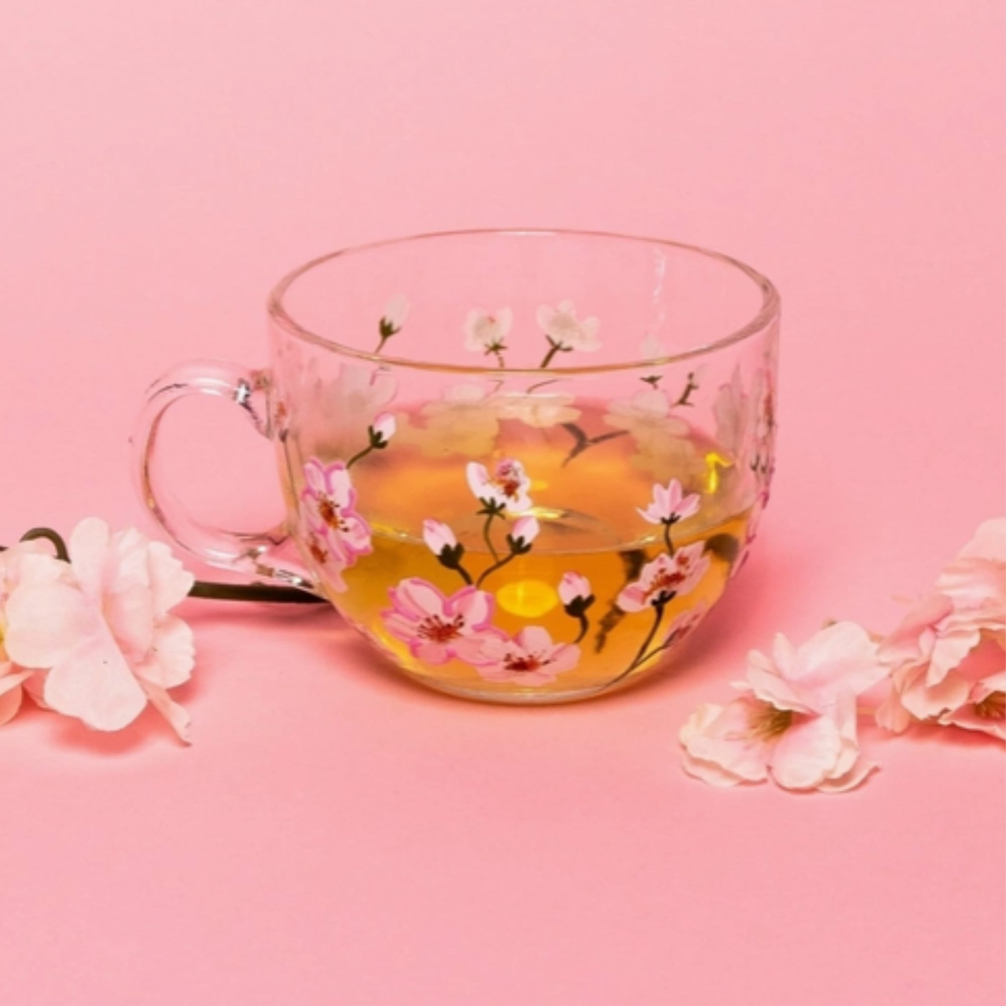 Clear glass teacup with pink floral print on a pink background